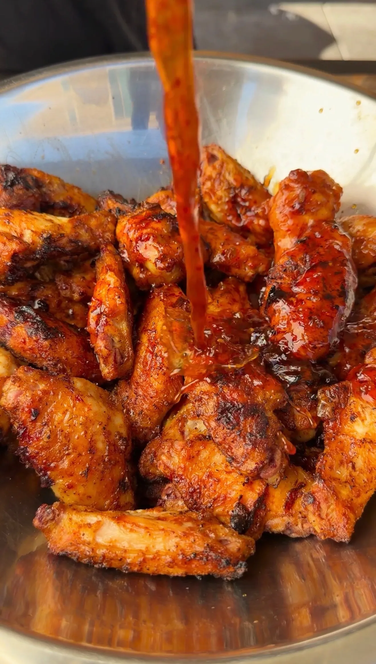 Crispy chicken wings in a steel bowl being drizzled with glossy honey garlic sauce
