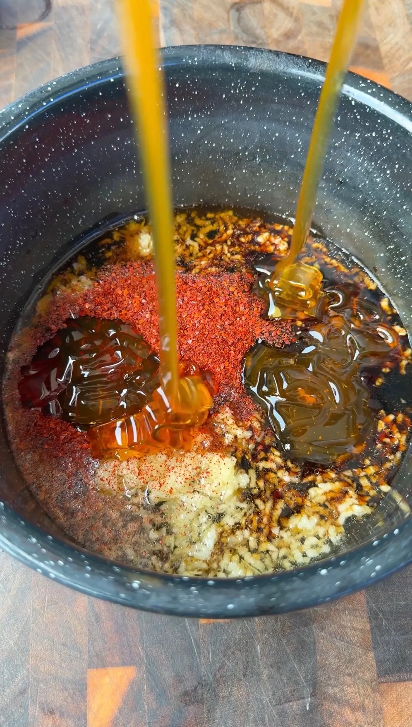 Honey being poured into a bowl with minced garlic, red chili powder, and soy sauce for wing marinade