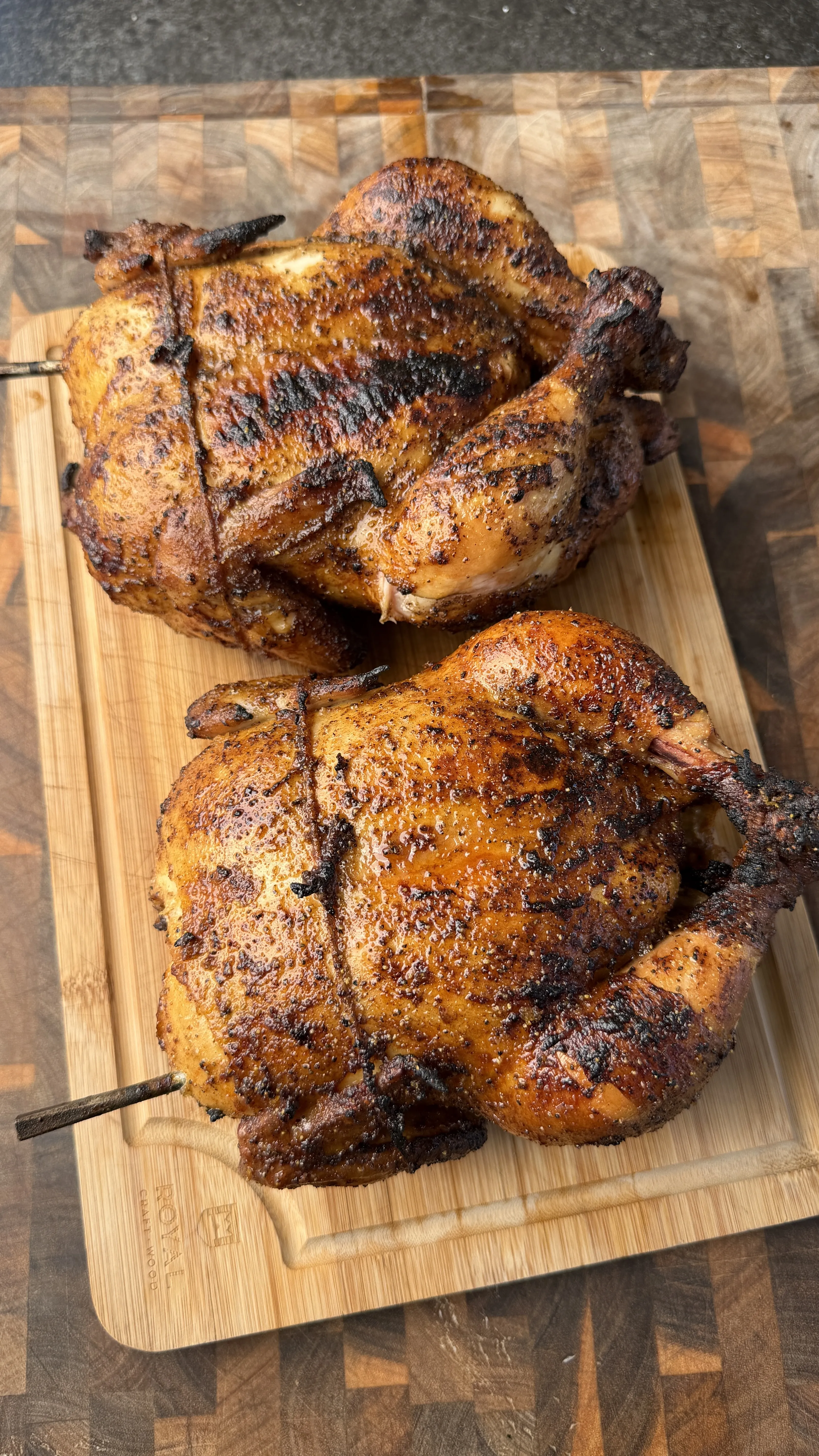 Two honey lemon pepper whole roasted chickens with golden-brown crispy skin on a wooden cutting board