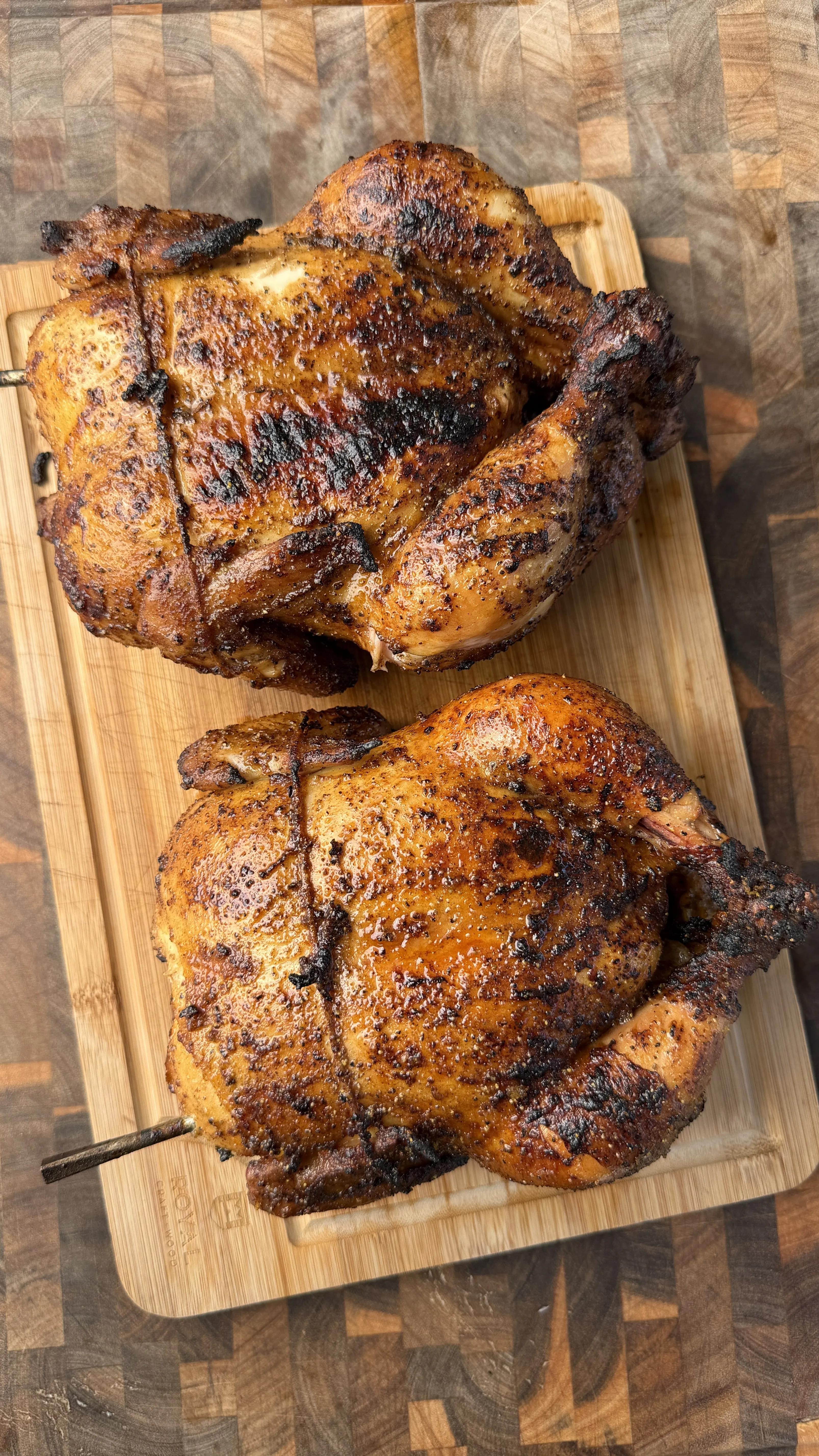 Two honey lemon pepper whole roasted chickens with golden-brown crispy skin on a wooden cutting board
