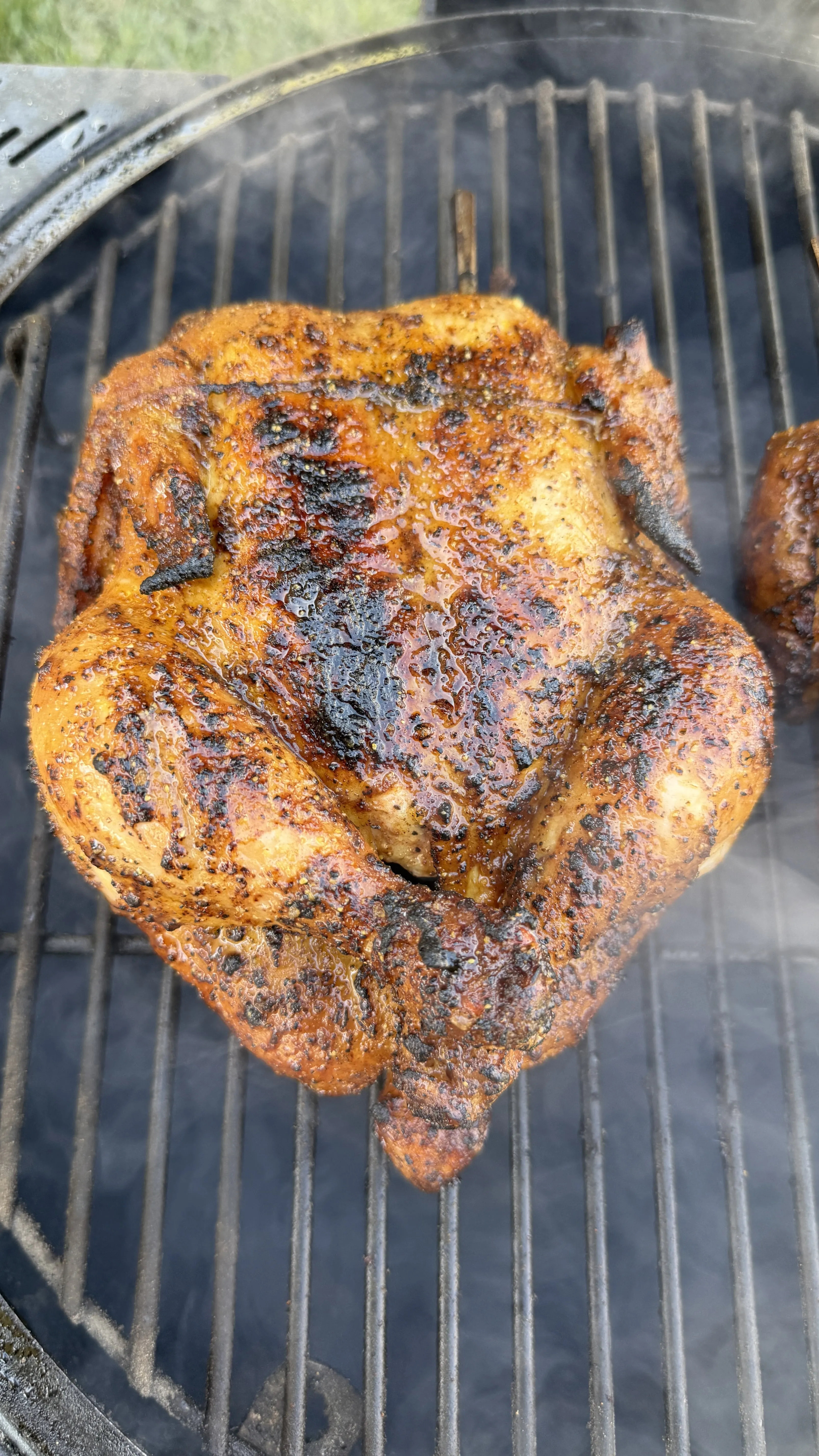 Whole honey lemon pepper chicken cooking on a charcoal grill with golden-brown, caramelized skin
