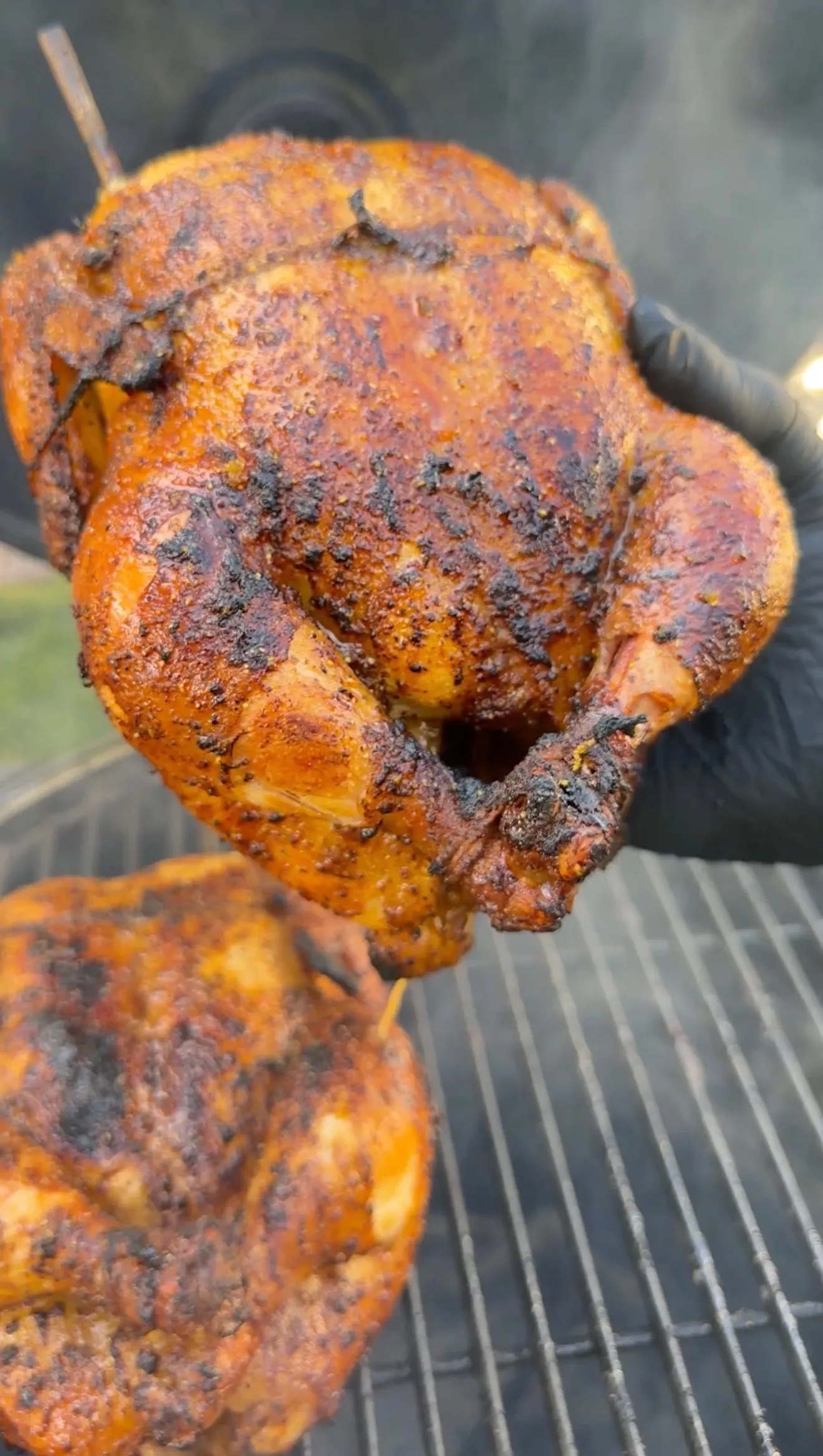 Whole smoked honey lemon pepper chicken with charred spice crust held over a grill grate