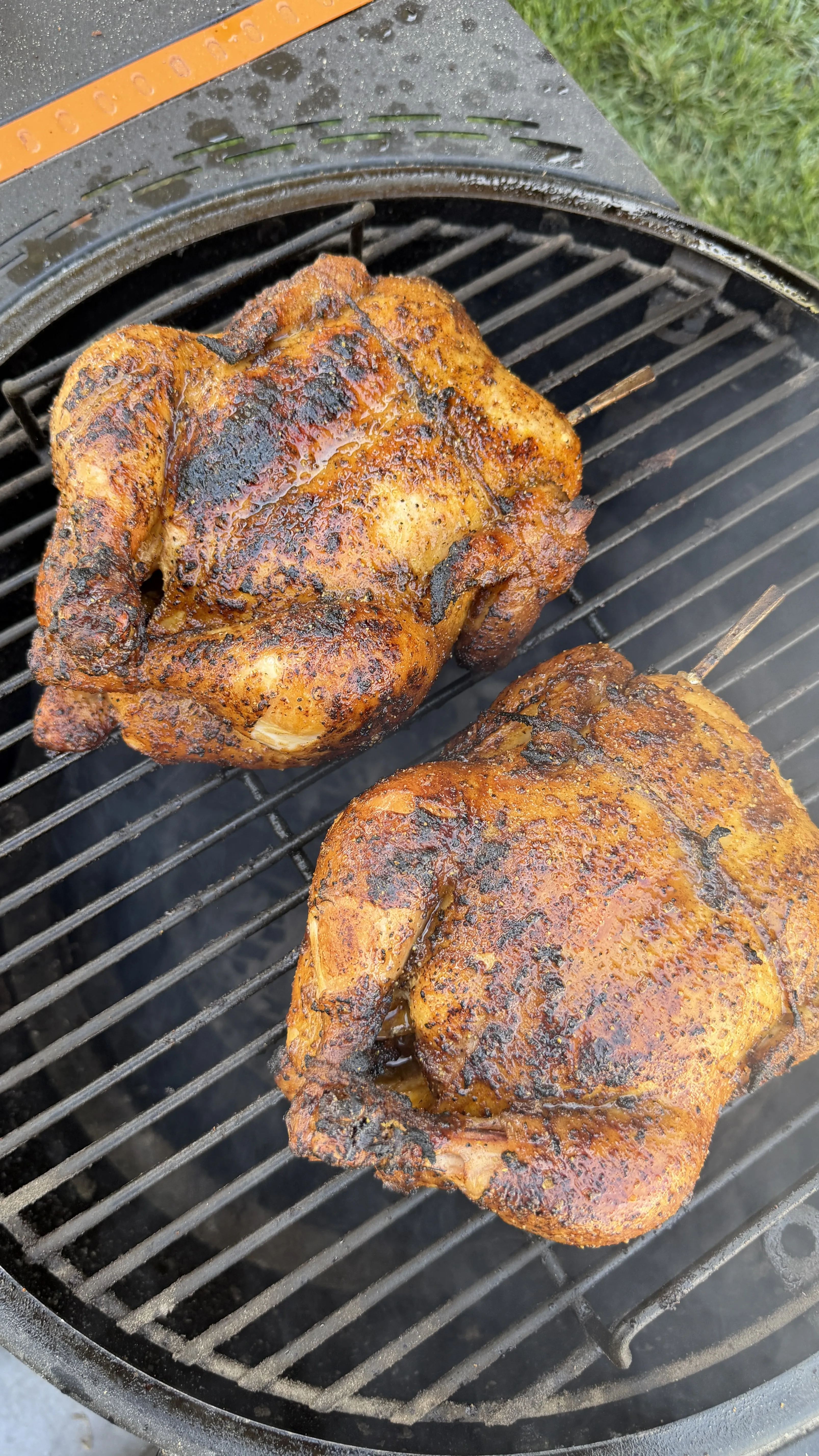 Two whole spice-rubbed honey lemon pepper chickens cooking on a round charcoal grill