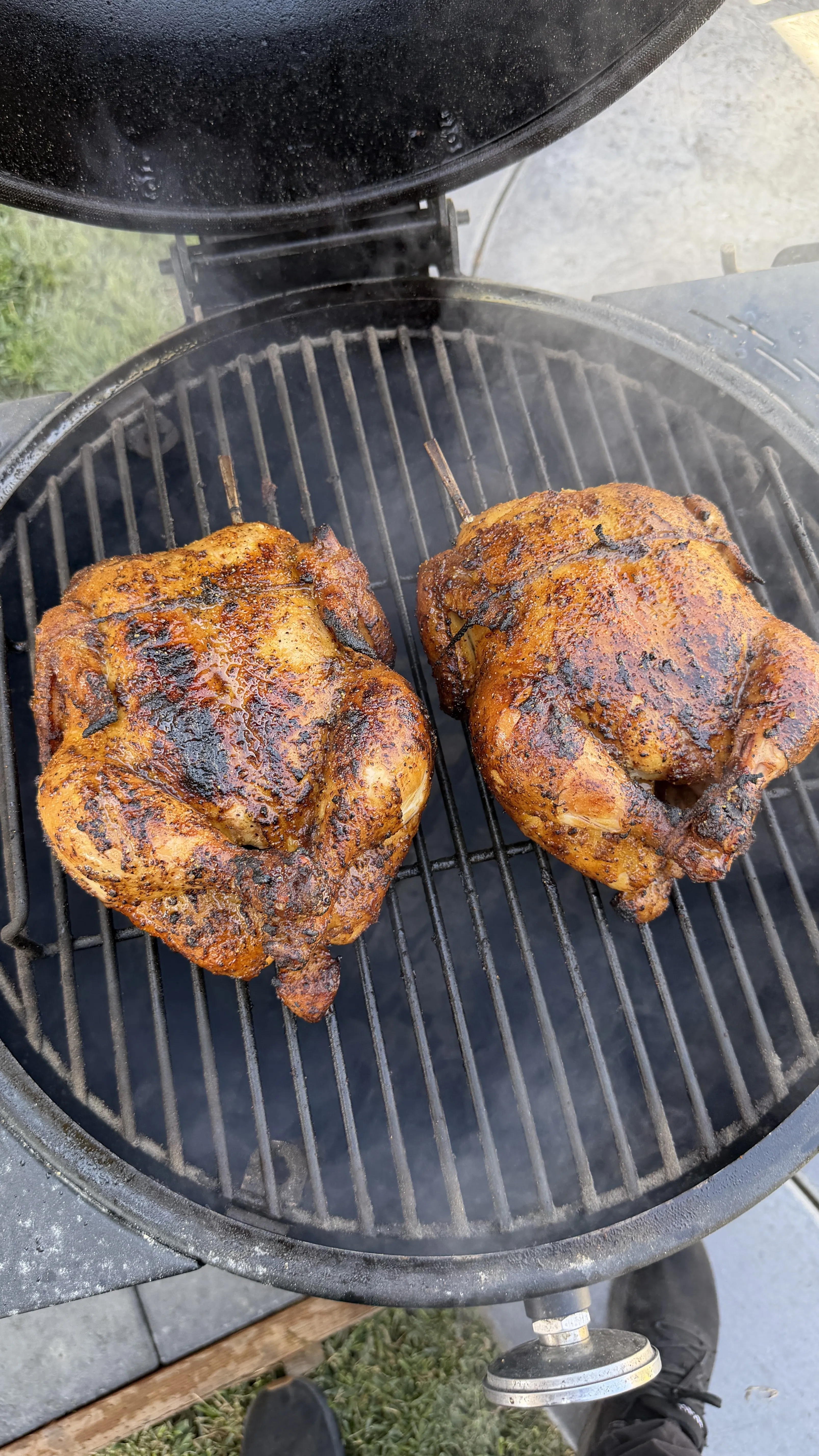 Two whole honey lemon pepper chickens with golden-brown crispy skin cooking on a charcoal kettle grill