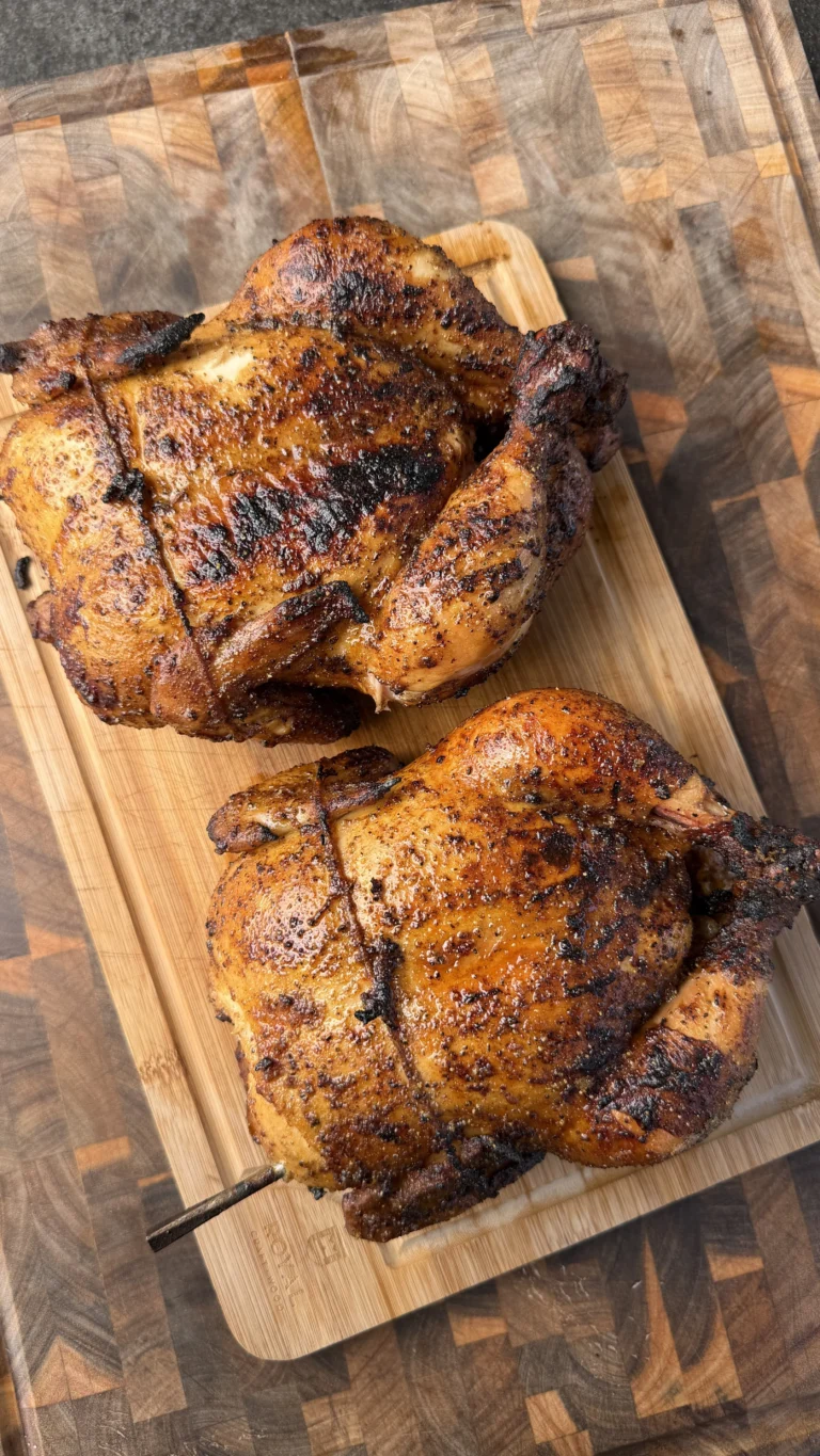 Two honey lemon pepper whole roasted chickens with caramelized skin on a wooden cutting board