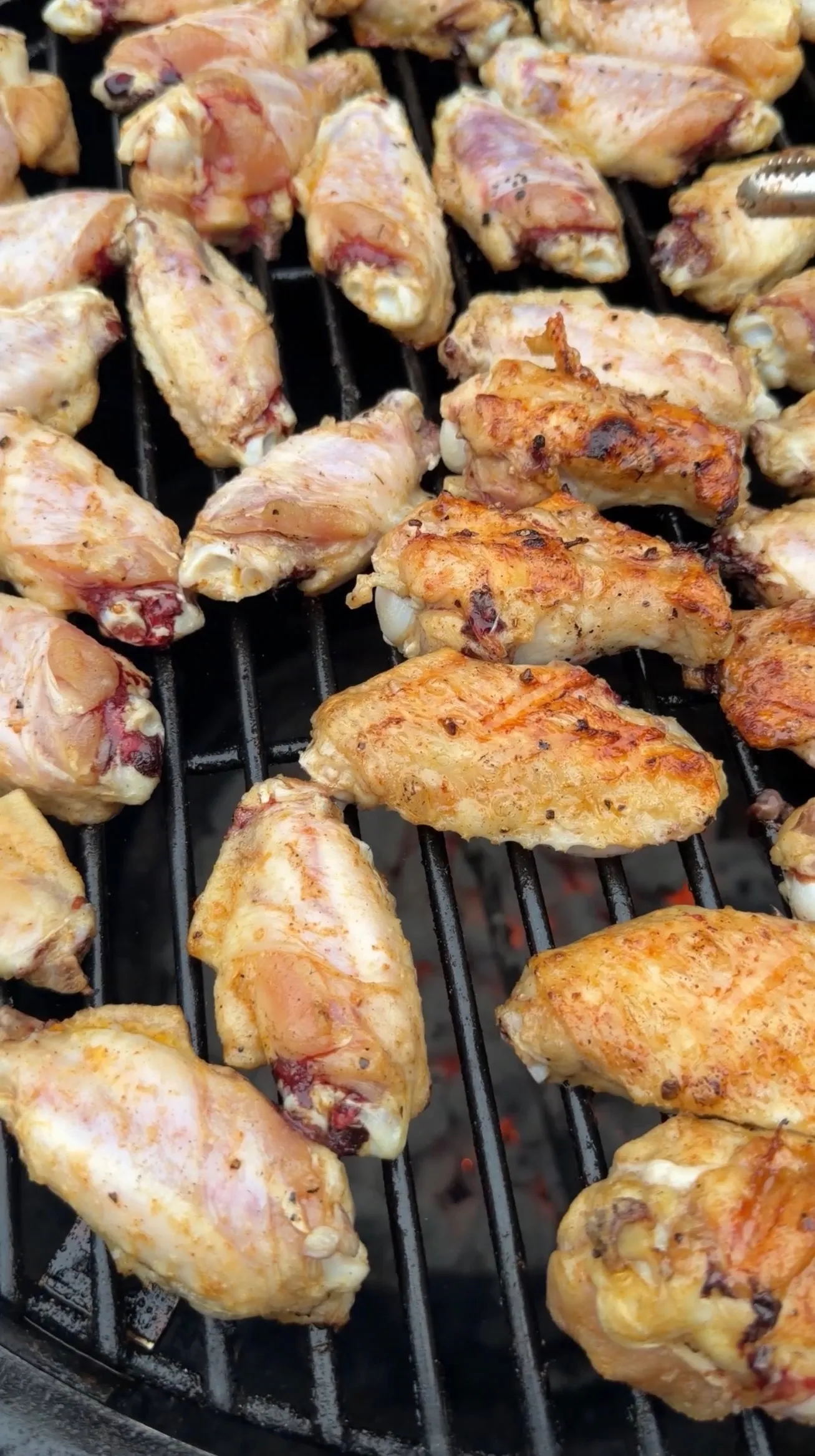 Hot sauce glazed chicken wings cooking on a charcoal grill, showing various stages of golden-brown caramelization