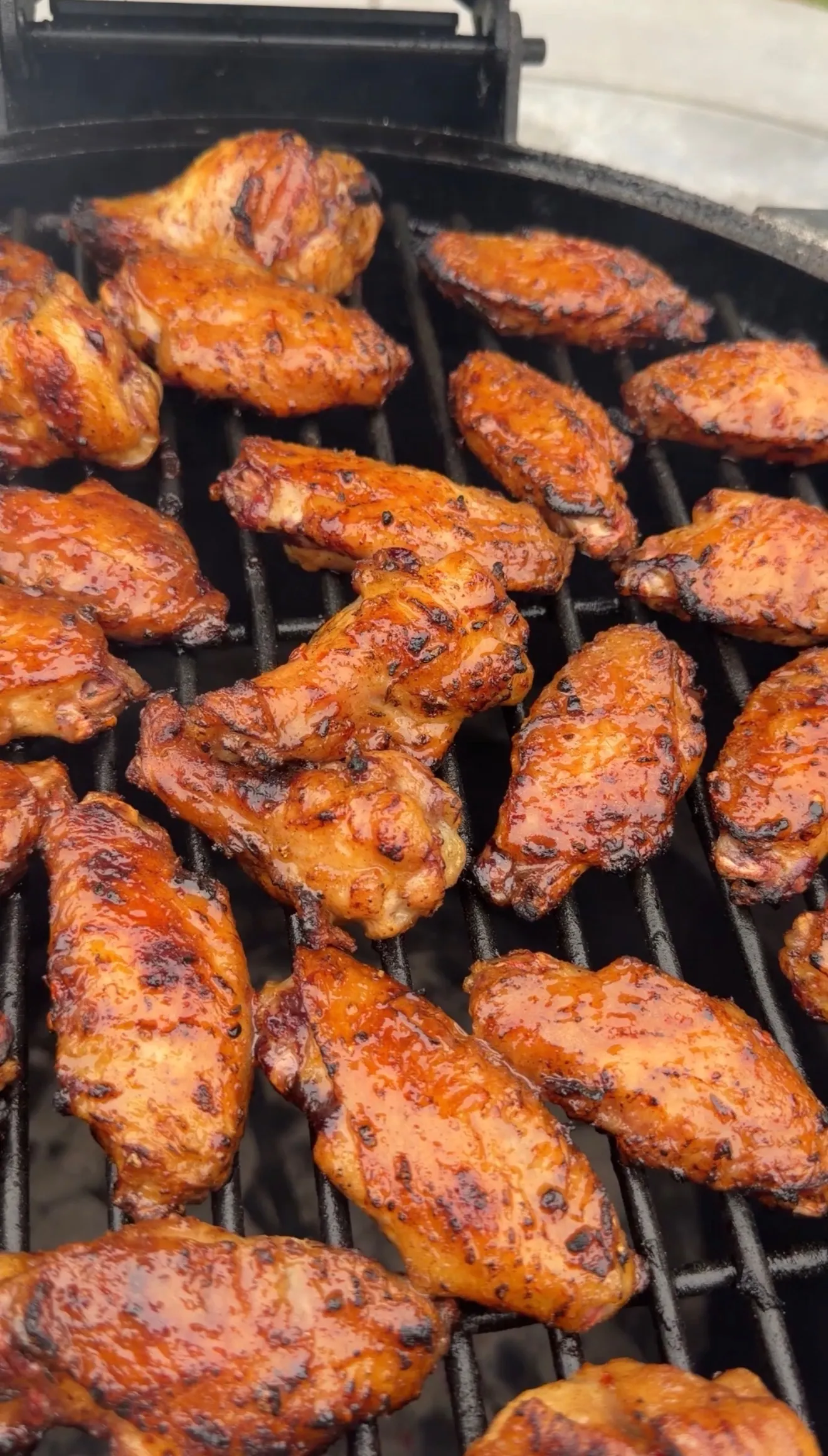 Sticky hot sauce glazed chicken wings grilling on a charcoal grill with caramelized edges