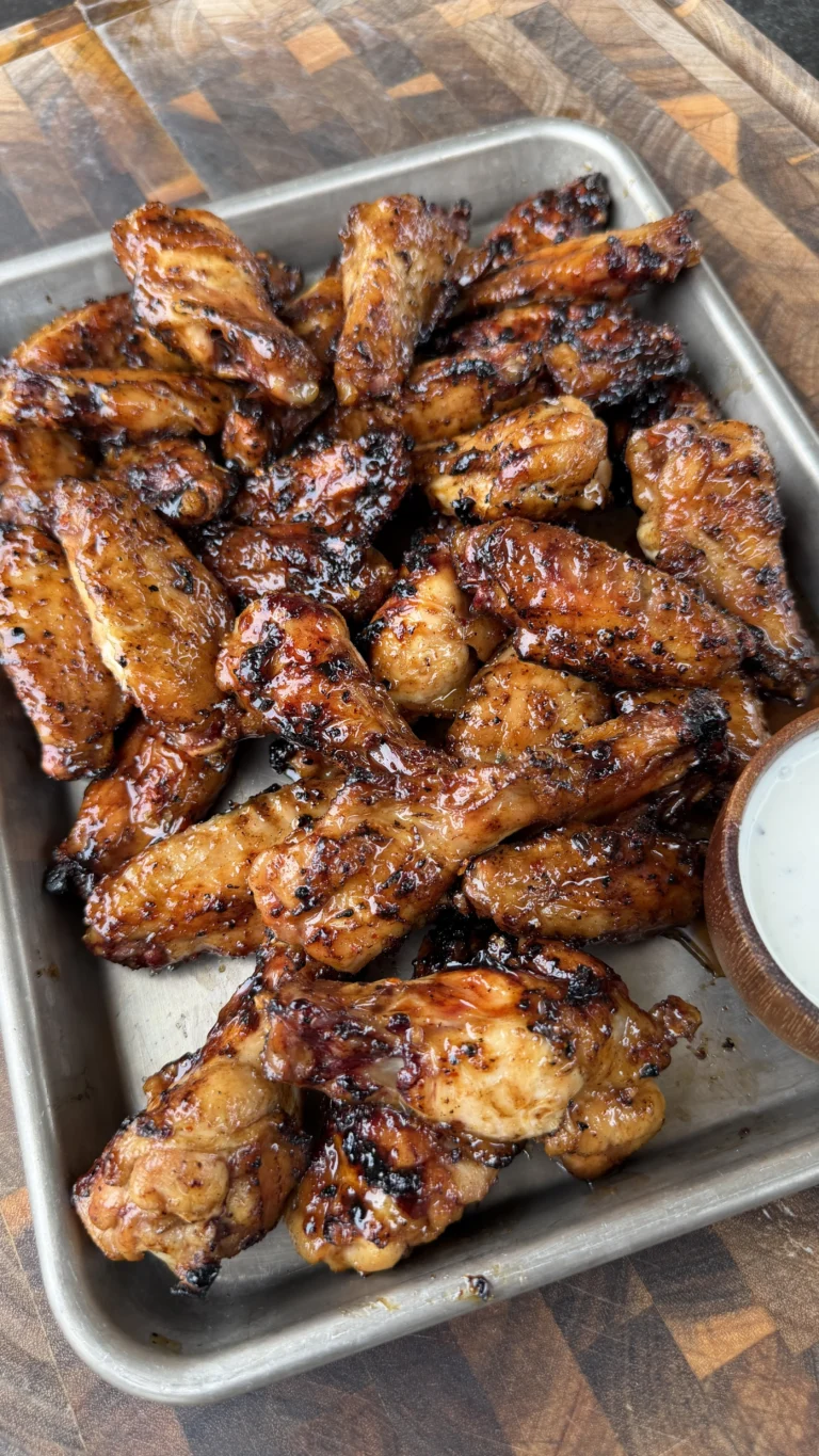 Caramelized hot sauce glazed chicken wings piled on a metal tray with a side of ranch dipping sauce