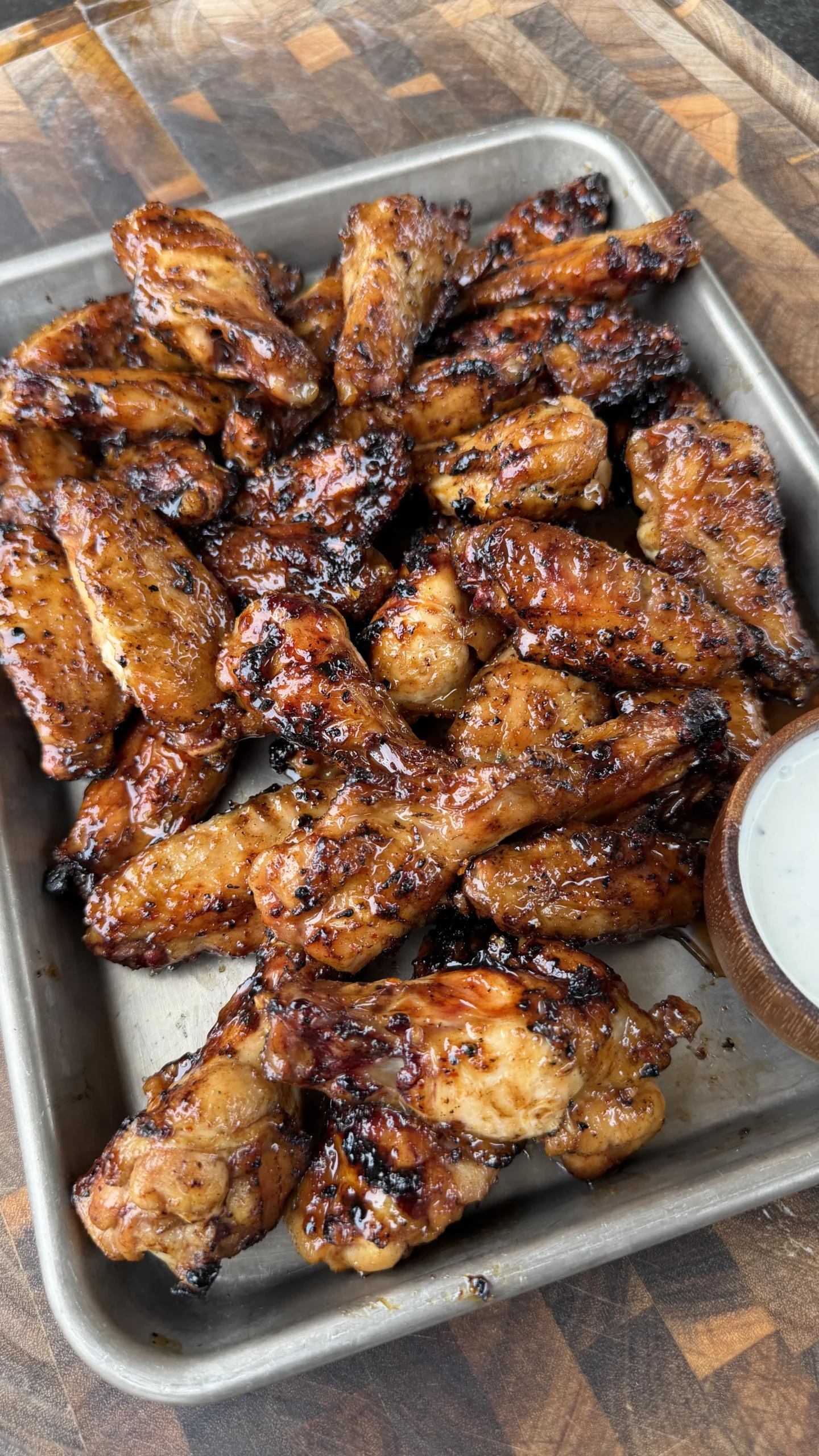 Caramelized hot sauce glazed chicken wings piled on a metal tray with a side of ranch dipping sauce
