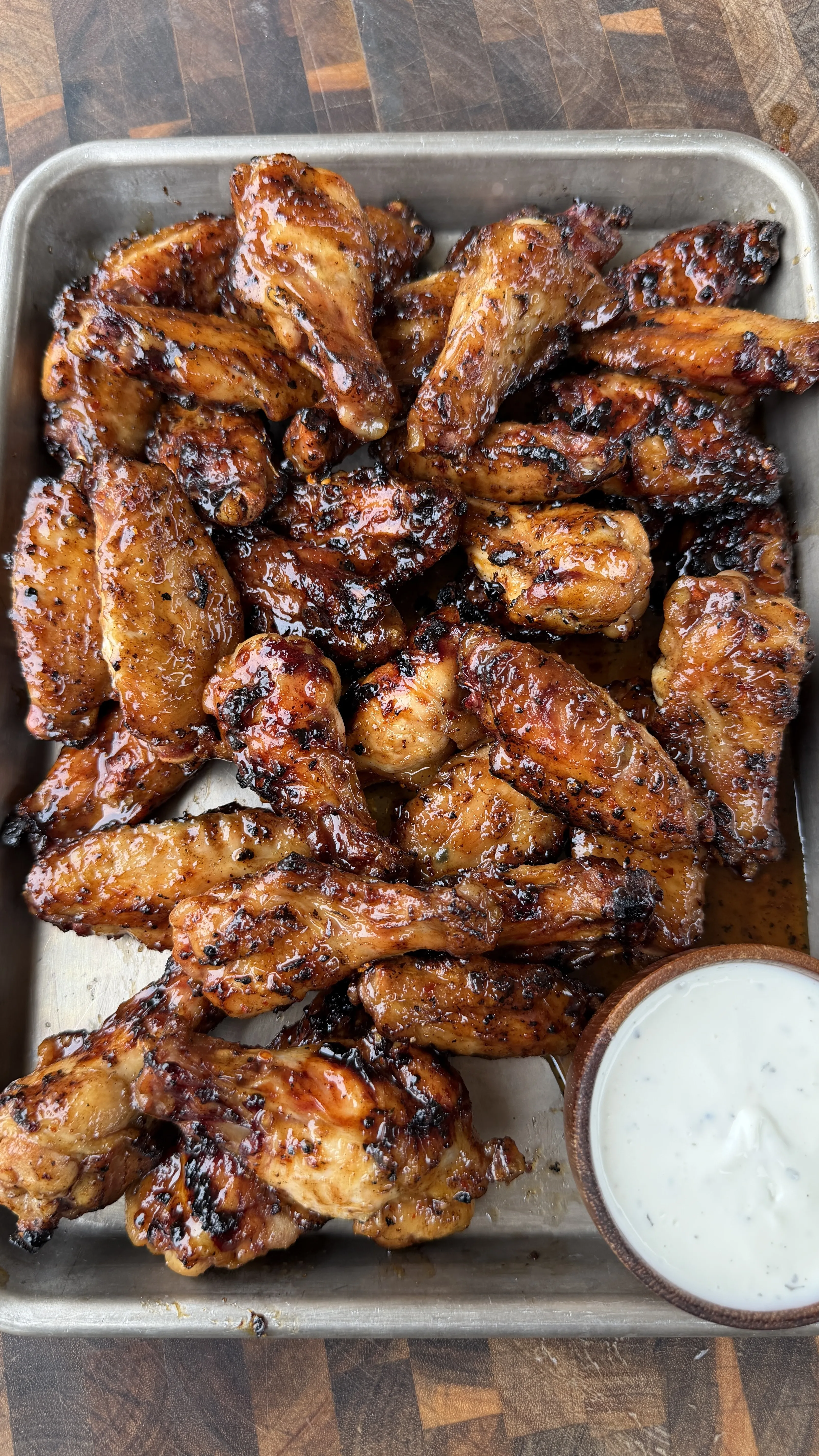 Caramelized hot sauce glazed chicken wings piled on a metal tray with a side of ranch dipping sauce