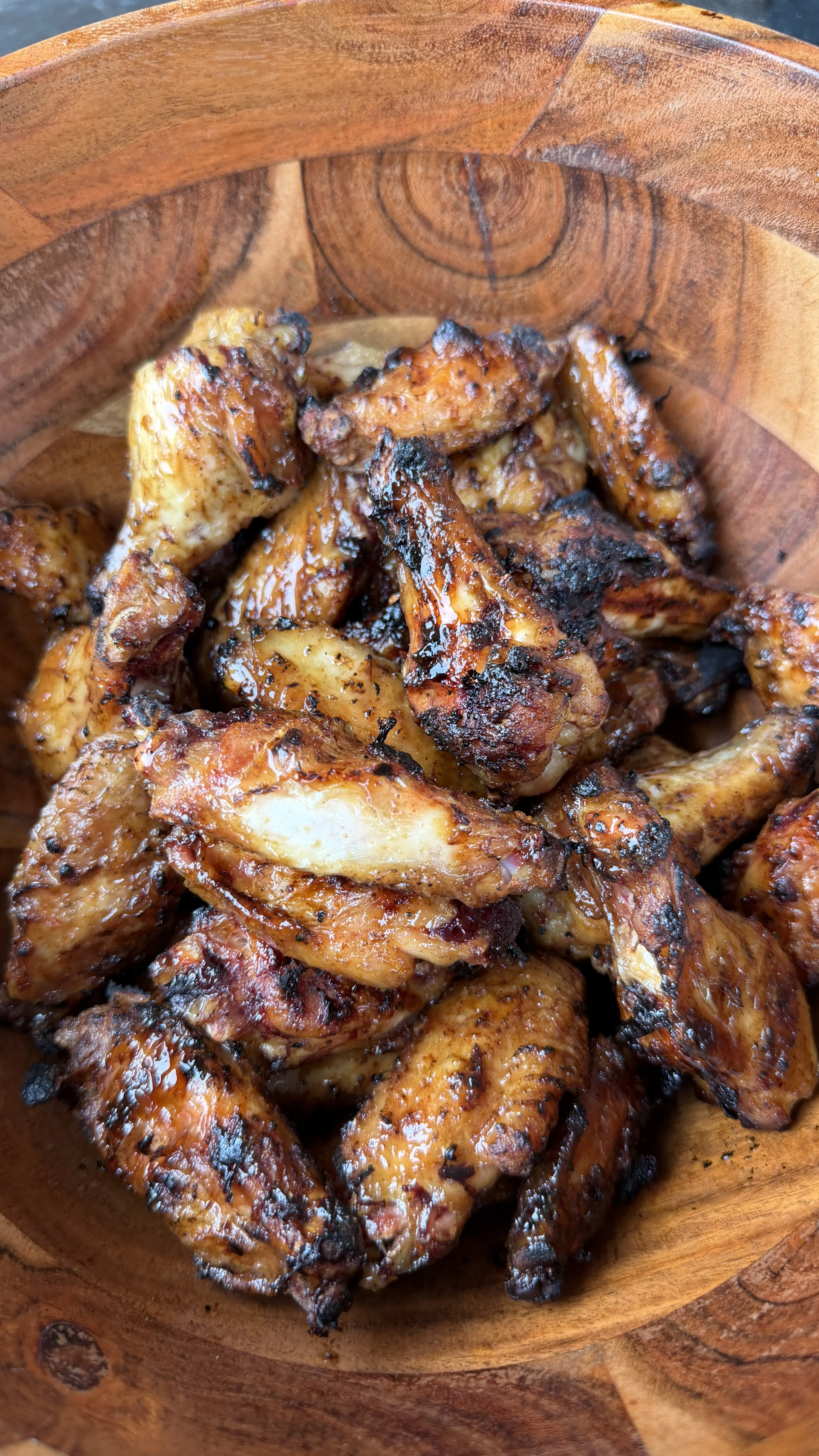 Crispy hot sauce glazed chicken wings piled high in a rustic wooden bowl with charred caramelized edges
