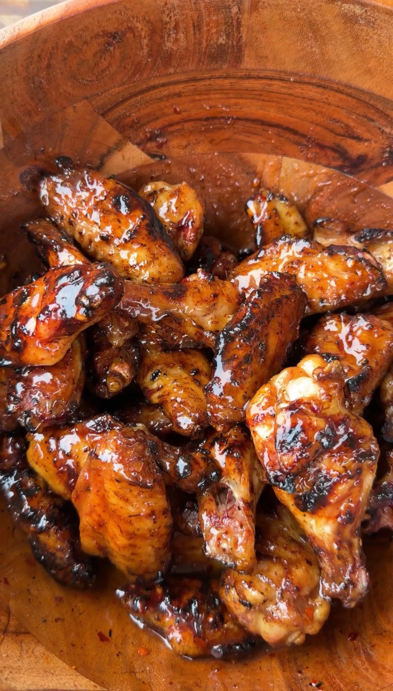 Glossy hot sauce glazed chicken wings piled high in a rustic wooden bowl with caramelized char marks