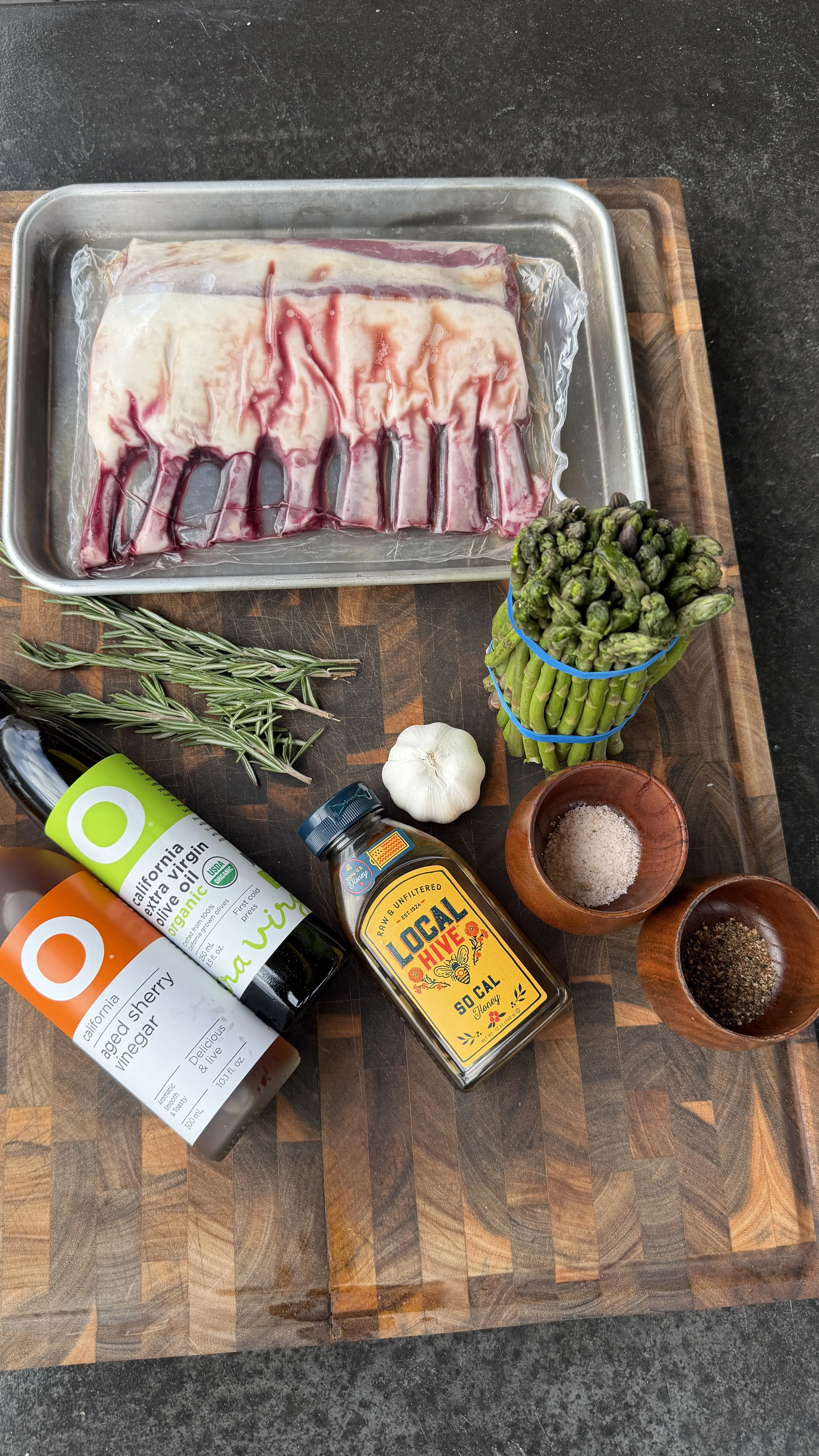 Rack of lamb with rosemary, garlic, olive oil, sherry vinegar, honey, asparagus, salt and pepper on a wood board