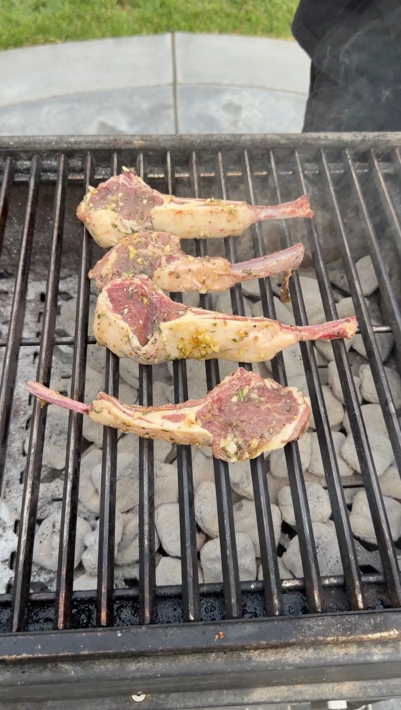 Four garlic and herb-marinated lamb lollipop chops cooking on a charcoal grill