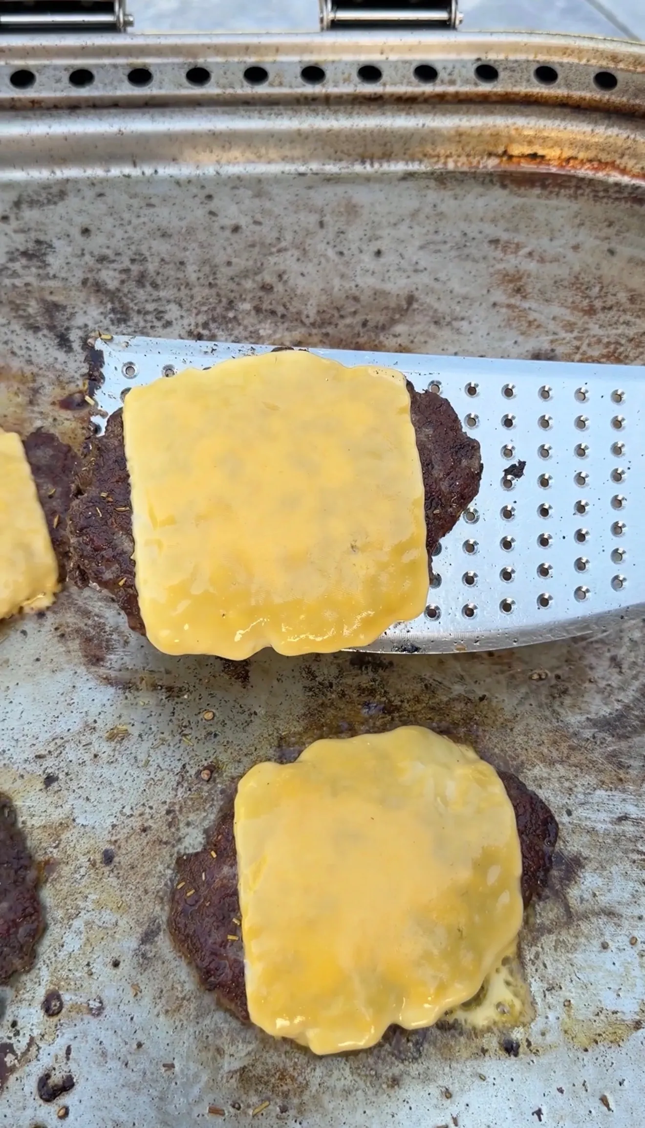 Juicy burger patties topped with melted American cheese cooking on a flat griddle for croissant burgers