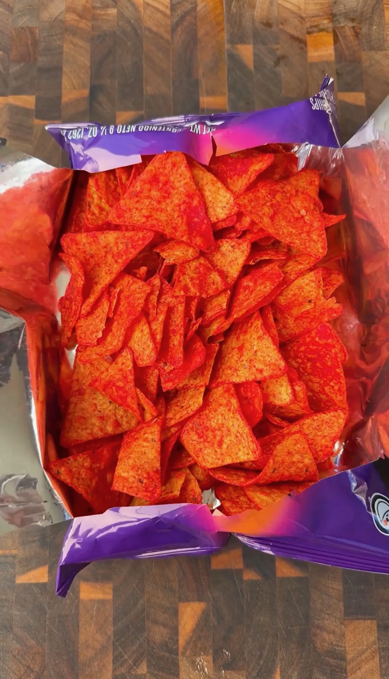 Open bag of red and orange Doritos tortilla chips viewed from above on a wooden surface
