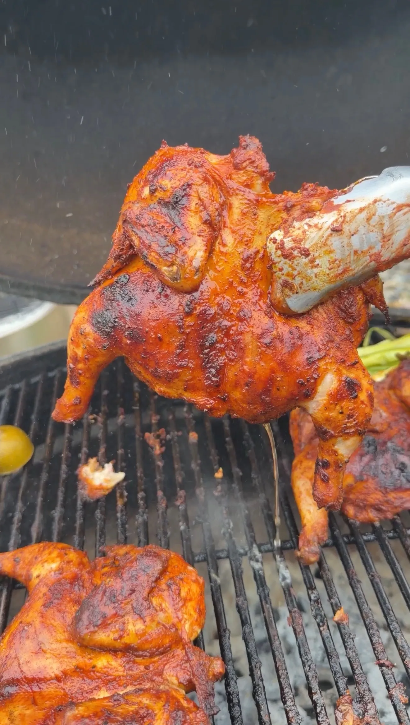 Spiced pollo asado style Cornish hen being lifted off charcoal grill, coated in vibrant red achiote marinade