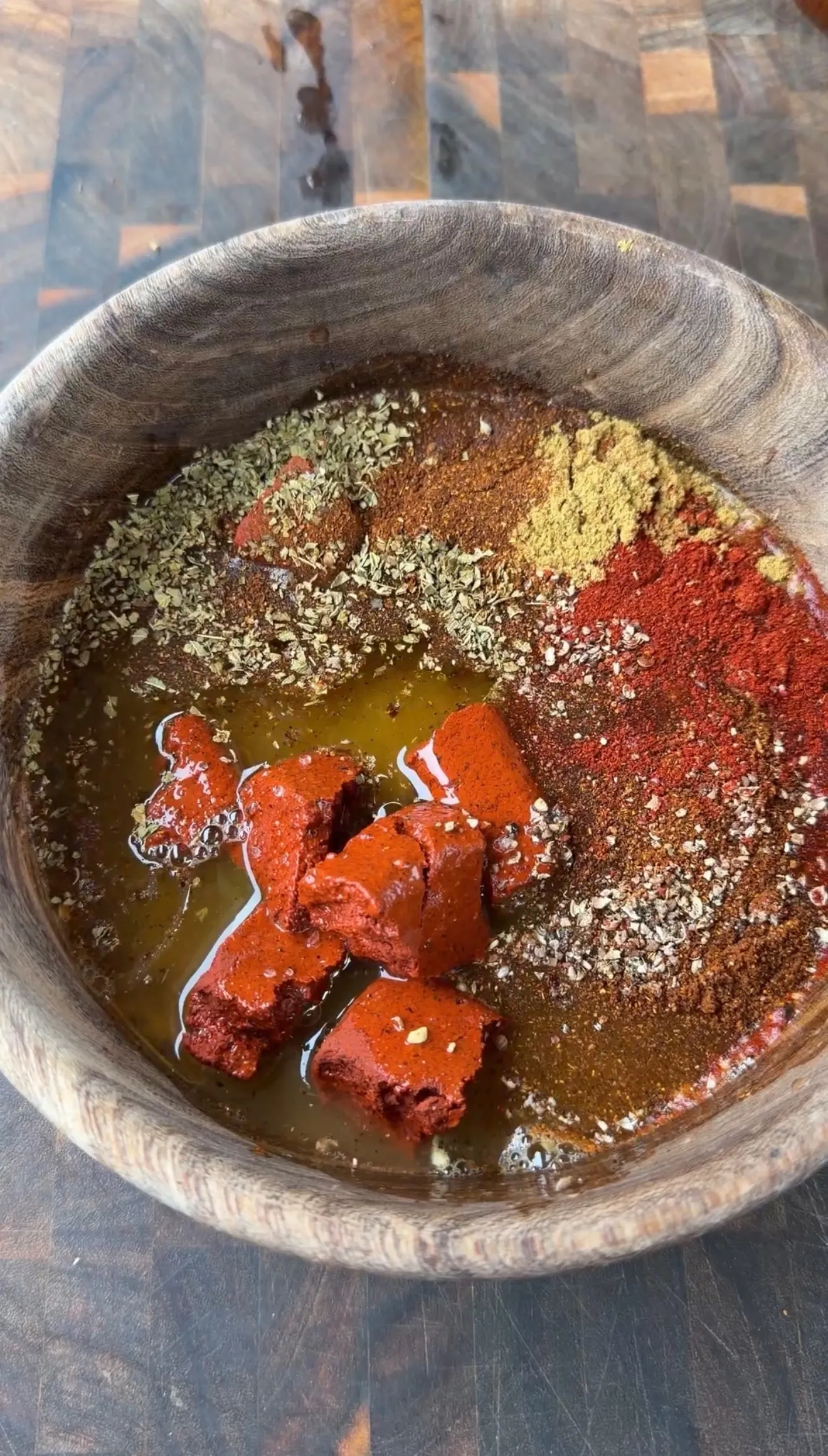 Wooden bowl with pollo asado marinade ingredients including achiote paste, paprika, cumin, oregano, and olive oil