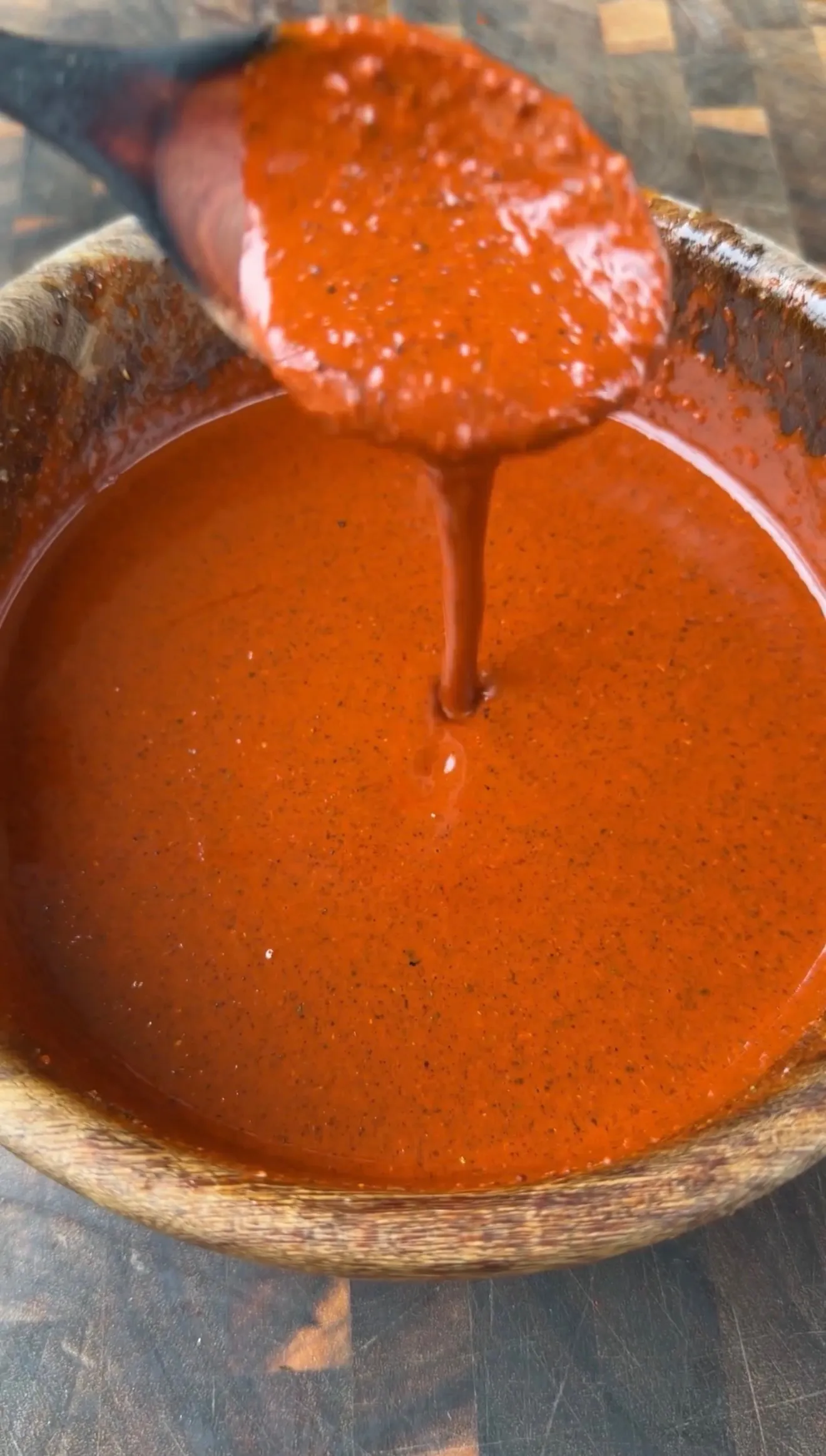 Rich red chile marinade for pollo asado dripping from a spoon into a rustic ceramic bowl