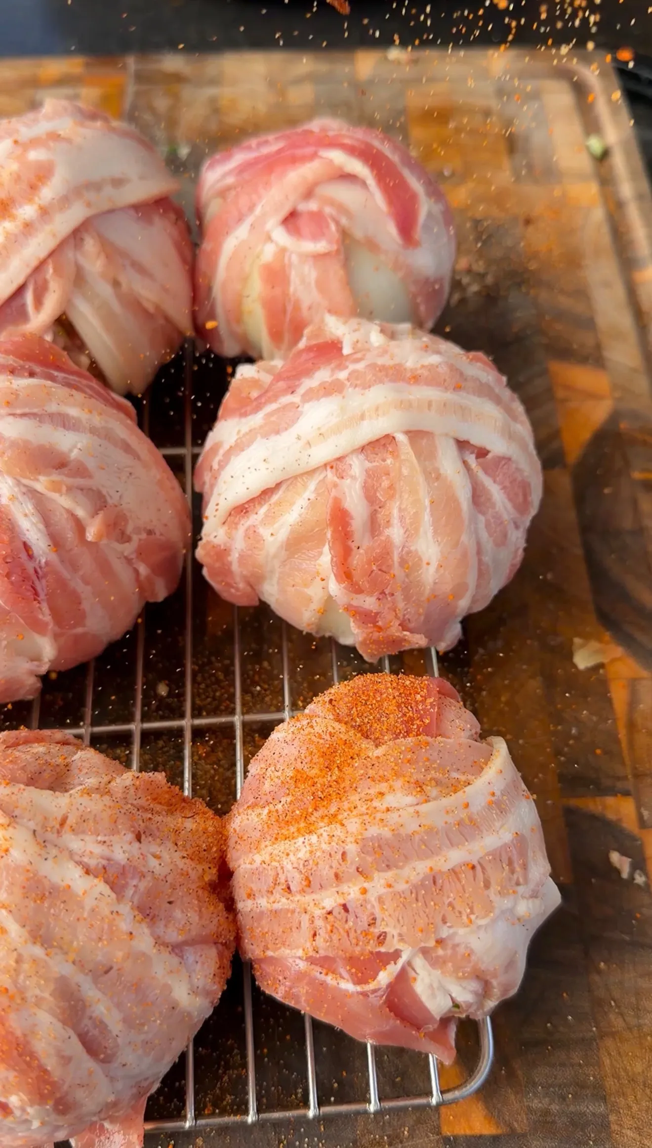 Raw bacon-wrapped onion bombs dusted with red seasoning on a wire rack before smoking