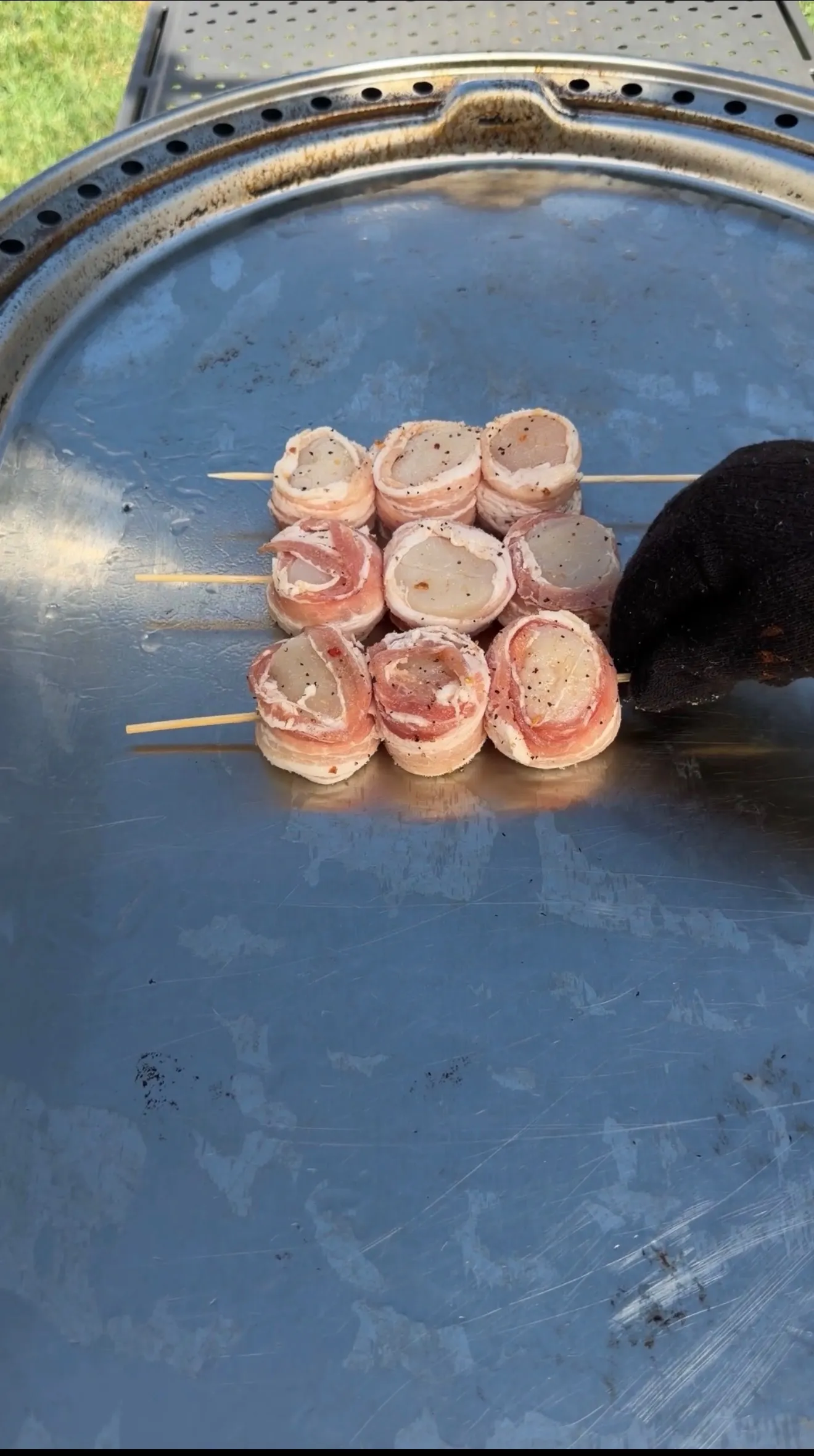 Raw bacon-wrapped scallops threaded on wooden skewers, seasoned with black pepper, ready to grill