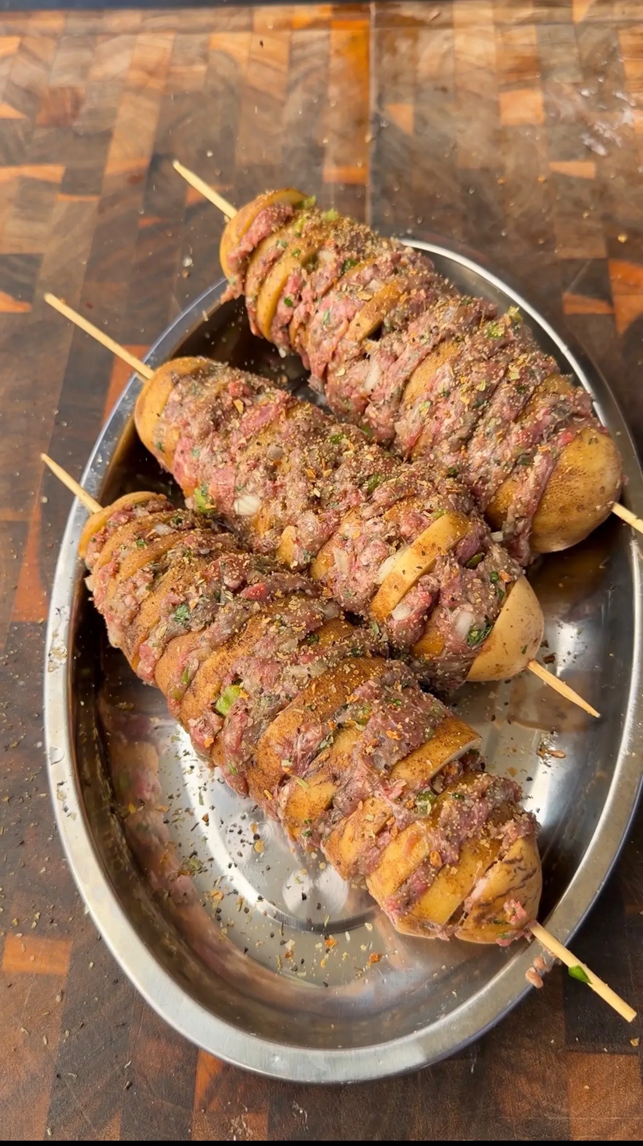 Raw Cajun butter potato beef kebabs on skewers, seasoned with herbs and spices, ready to grill on a metal tray