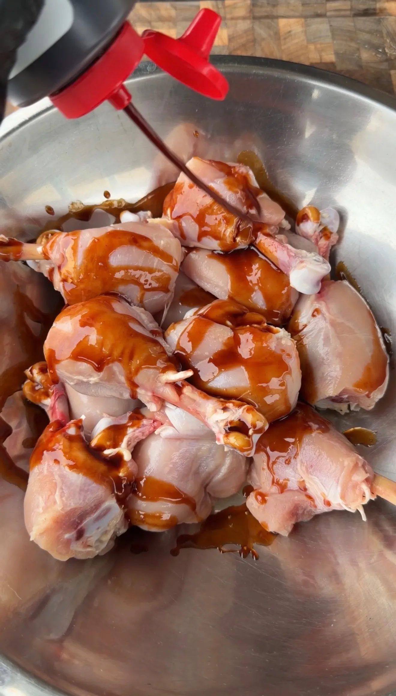 Raw chicken lollipops coated in spicy BBQ marinade in a stainless steel mixing bowl
