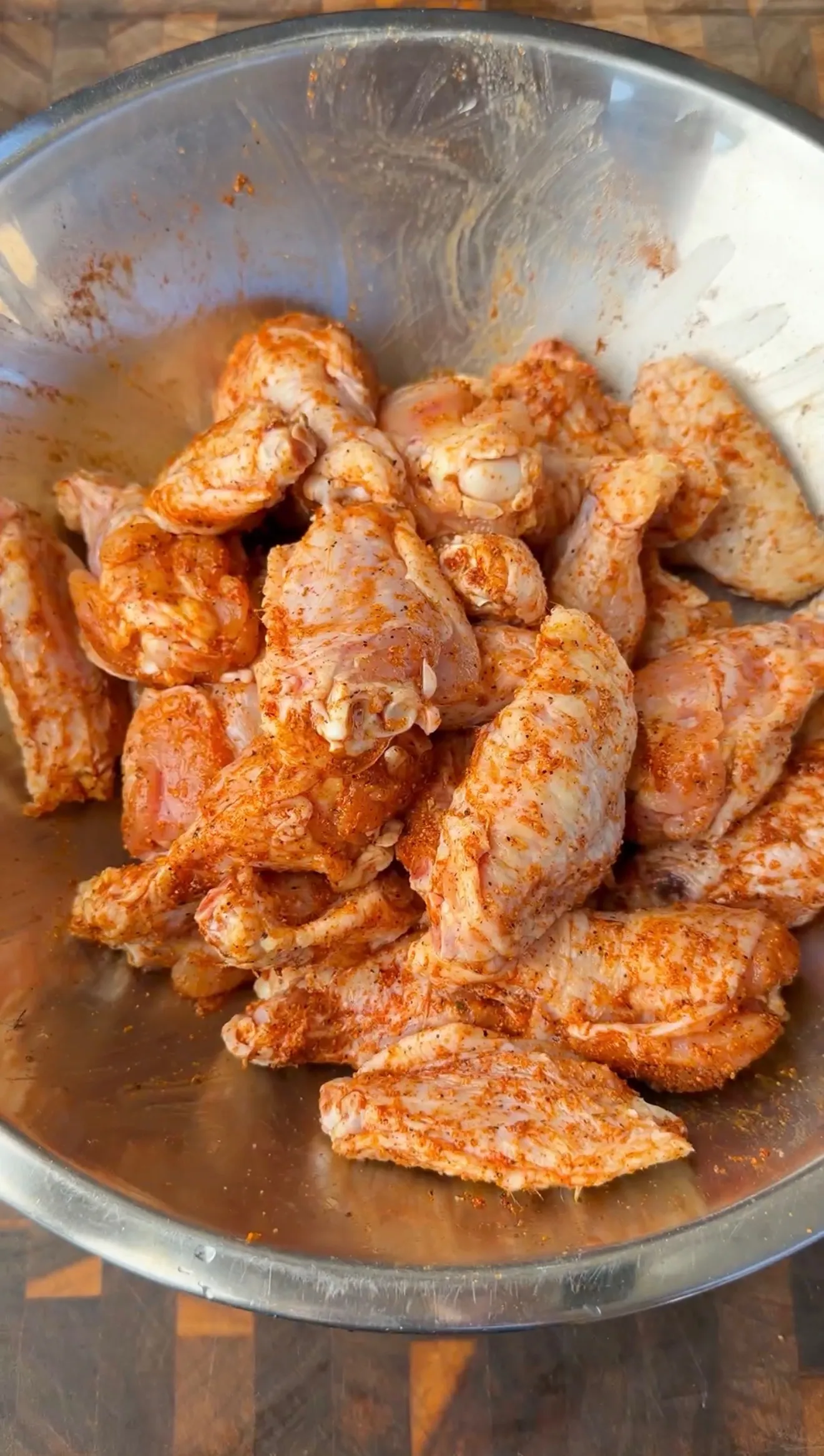 Raw chicken wings coated in red spice rub in a stainless steel mixing bowl, ready for honey garlic recipe