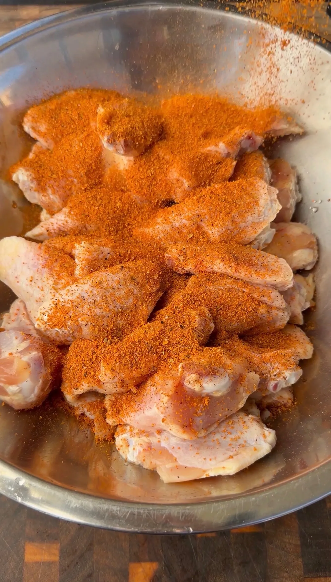 Raw chicken wings in a stainless steel bowl generously coated with red spice seasoning blend