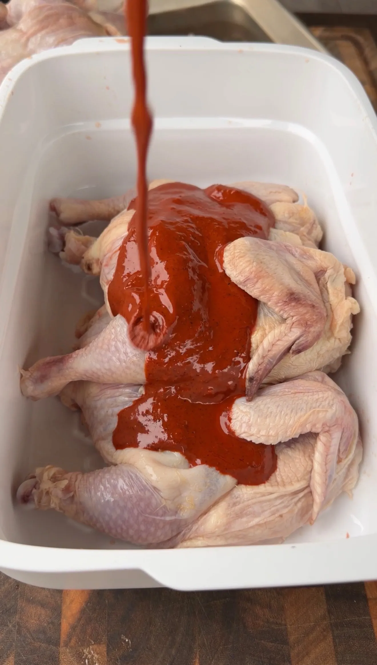 Red chile marinade being poured over raw Cornish hens in a white baking dish for Pollo Asado