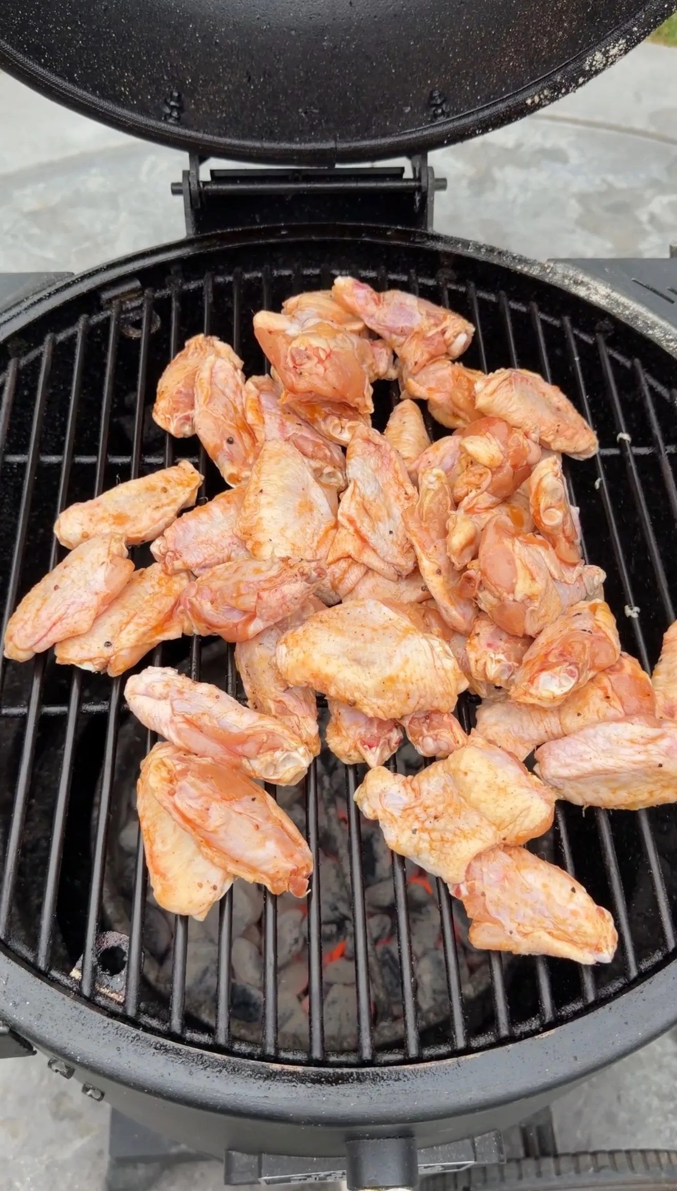 Raw marinated chicken wings piled on a round charcoal kettle grill, ready to cook