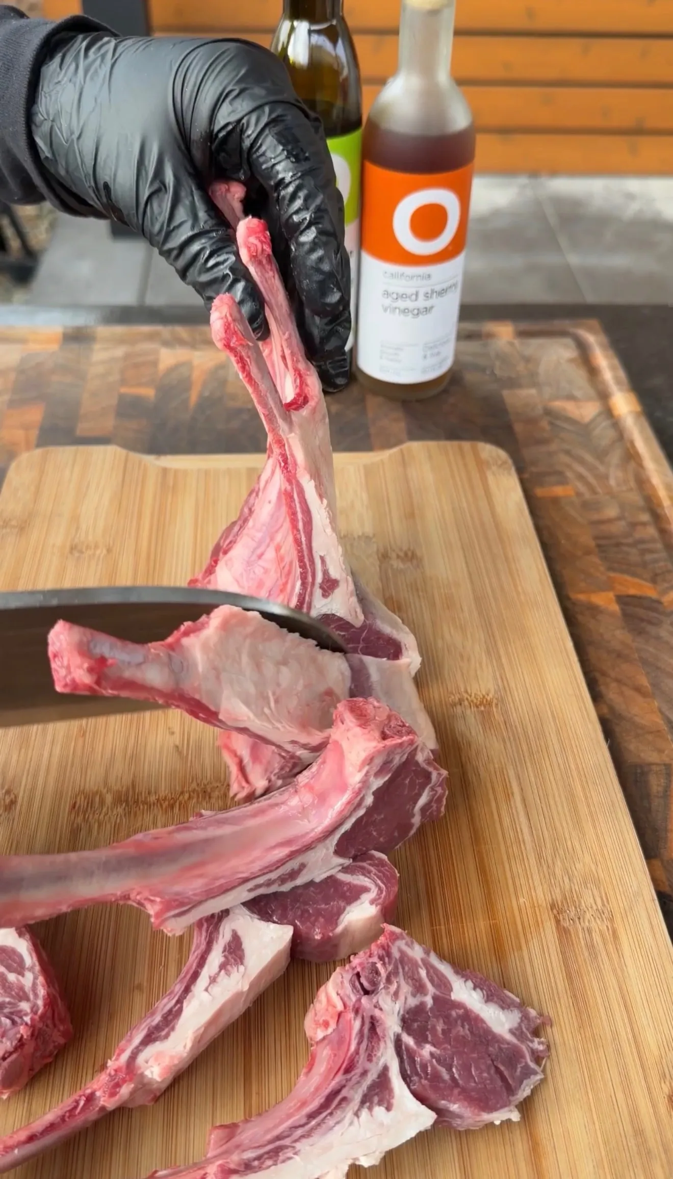 Raw lamb lollipop chops being separated on a wooden cutting board with aged sherry vinegar in background
