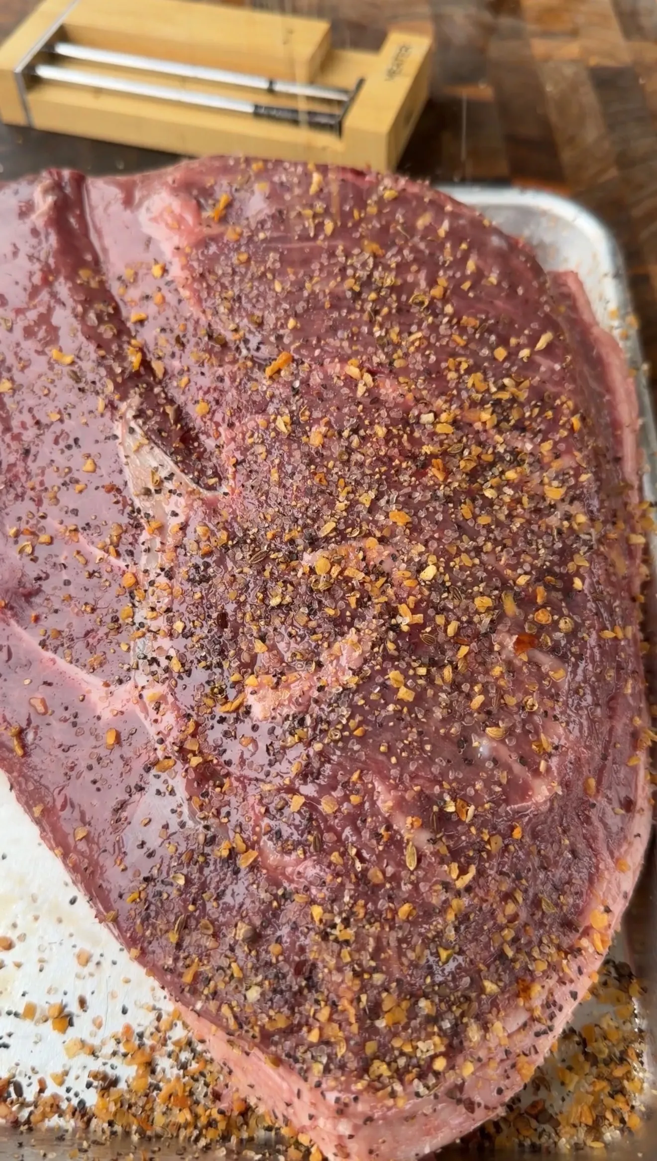 Raw picanha roast generously coated with cracked pepper, garlic, and spice rub on a sheet pan