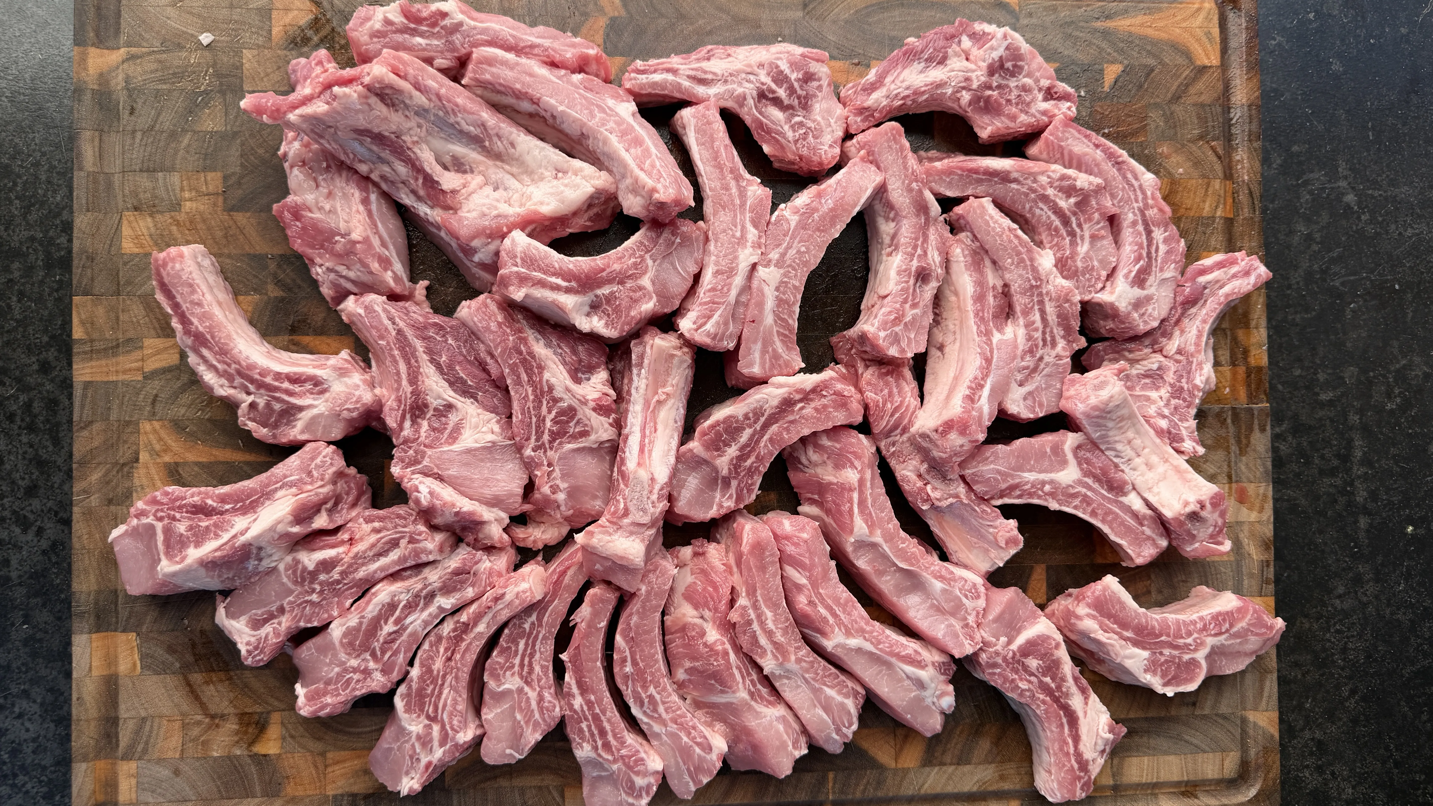 Individual raw pork rib pieces cut and spread across a wooden butcher block cutting board