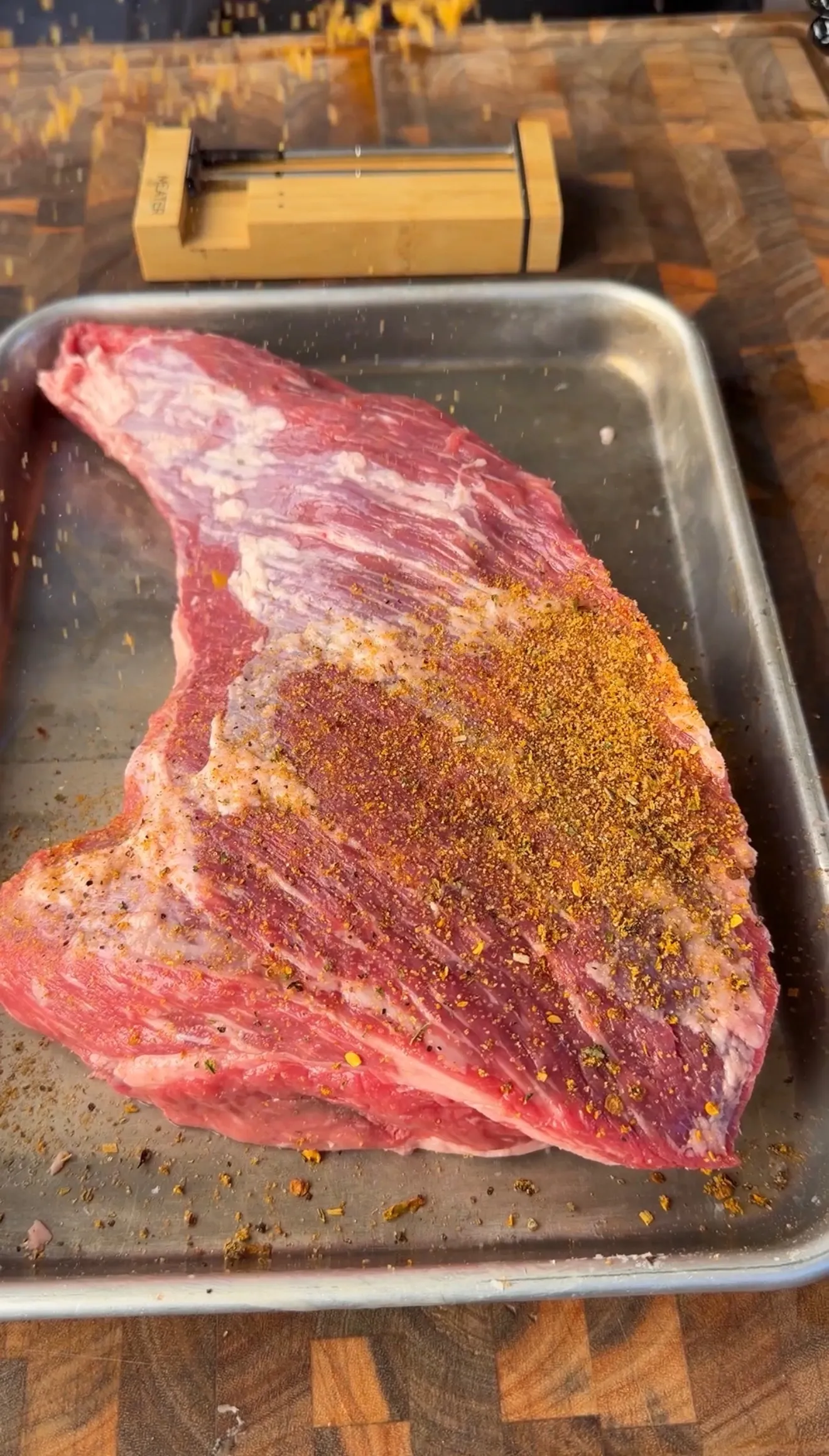 Raw tri-tip roast generously coated with spiced dry rub seasoning on a stainless steel baking pan