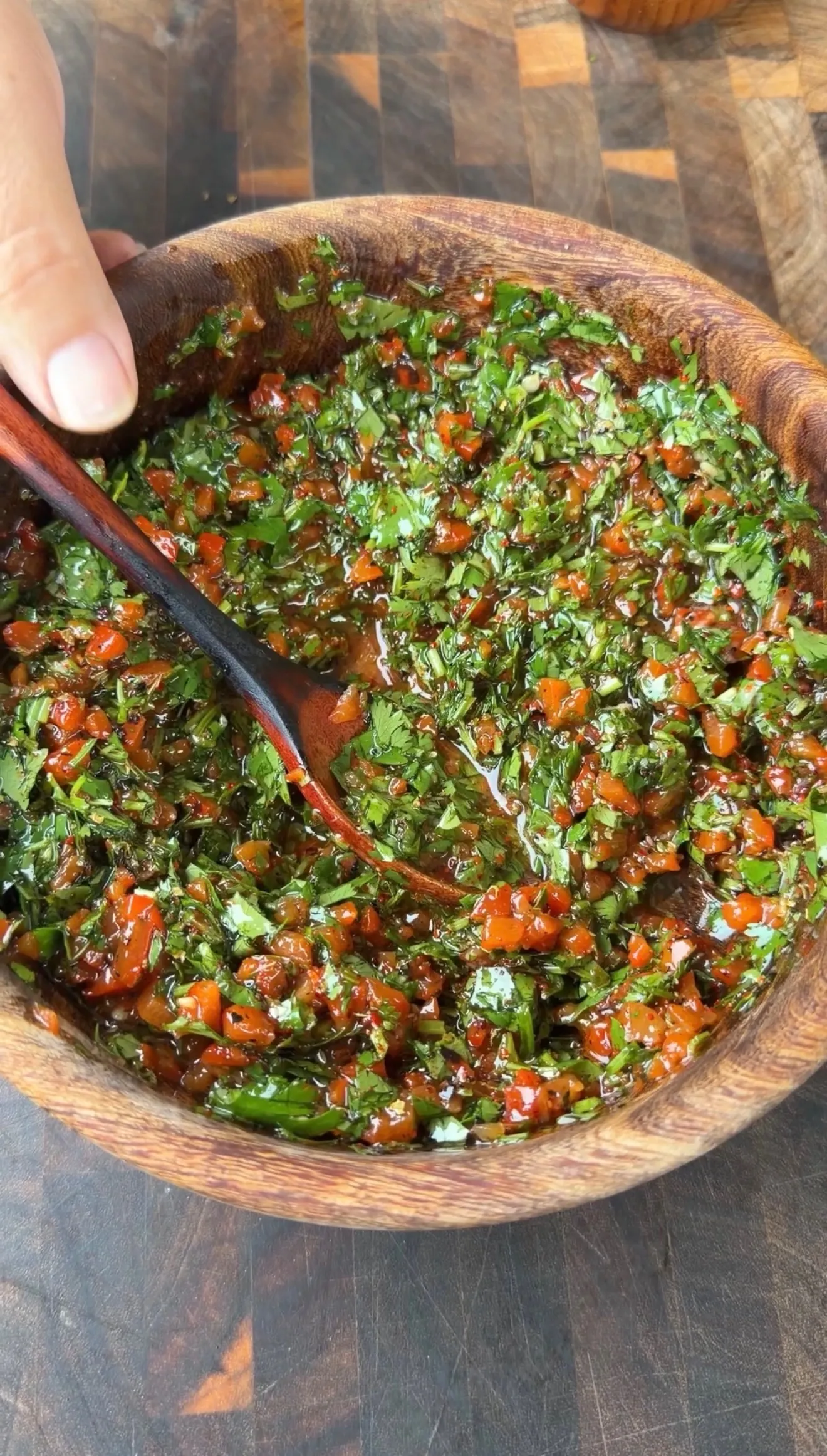 Fresh red cilantro chimichurri sauce with chopped herbs and chili in a rustic wooden bowl, stirred with a wooden spoon