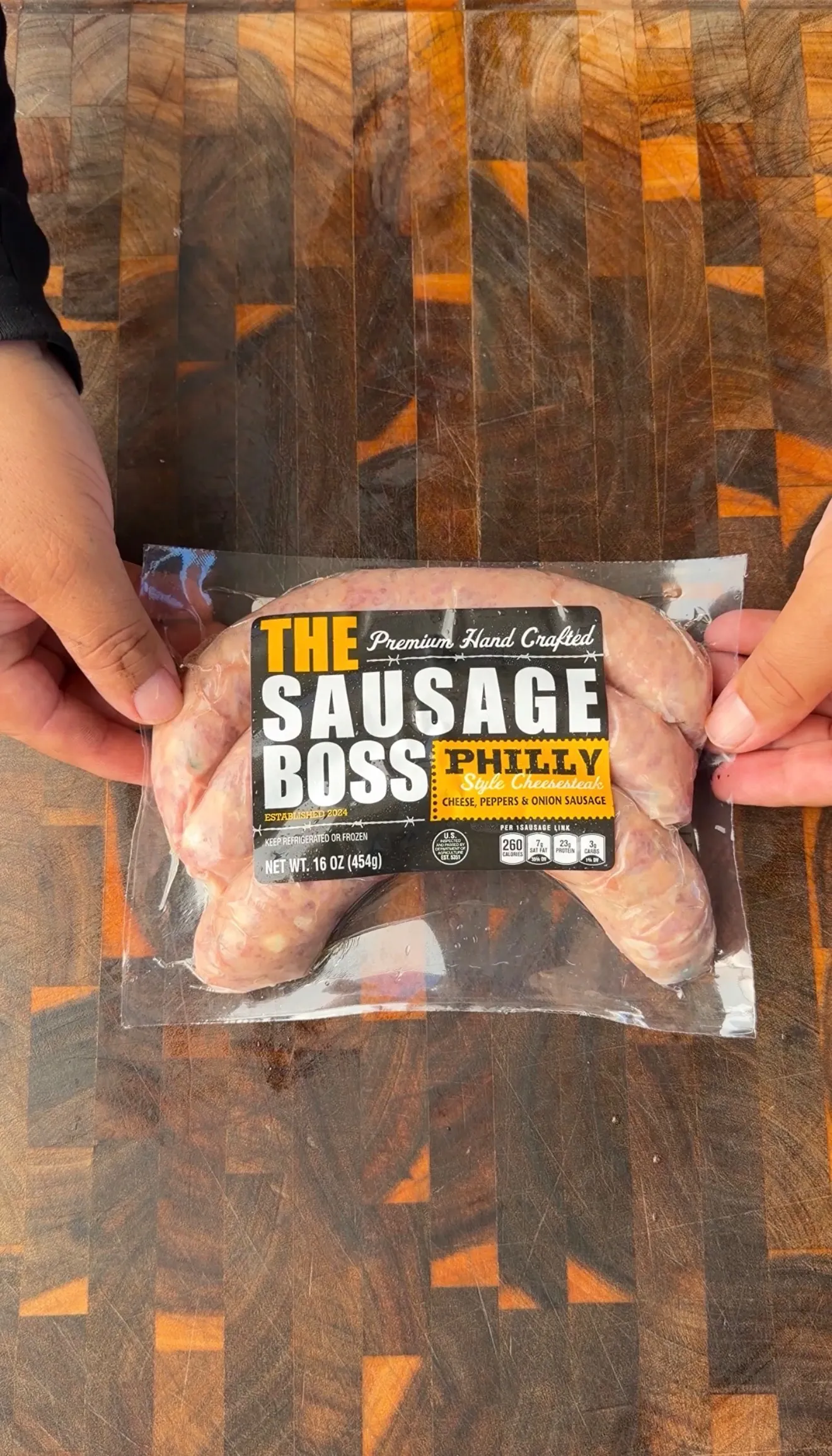 Package of The Sausage Boss Philly Style Cheesesteak sausage links held over a wooden cutting board