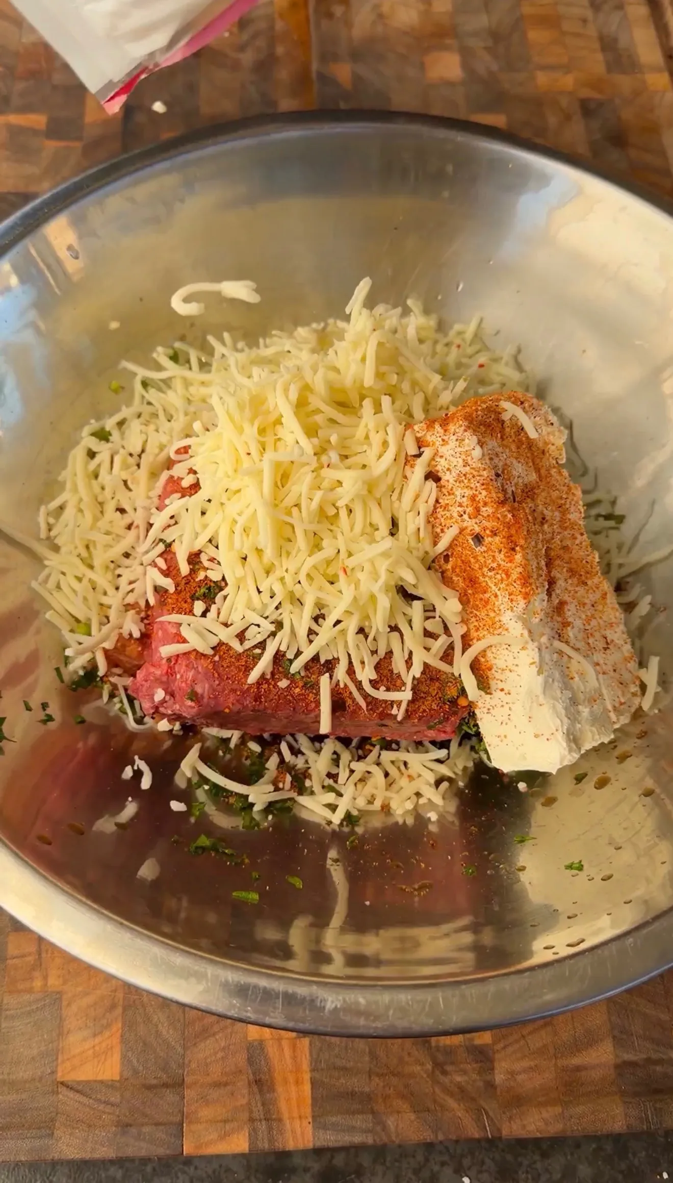 Seasoned ground beef with shredded mozzarella, spices, and herbs in a stainless steel mixing bowl