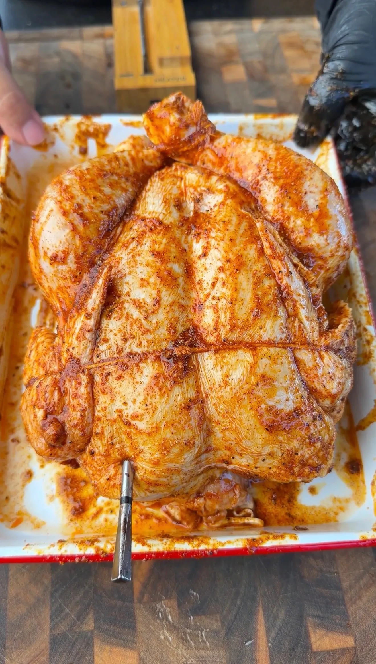 Raw whole chicken rubbed with honey lemon pepper seasoning in a white enamel roasting pan with a meat thermometer