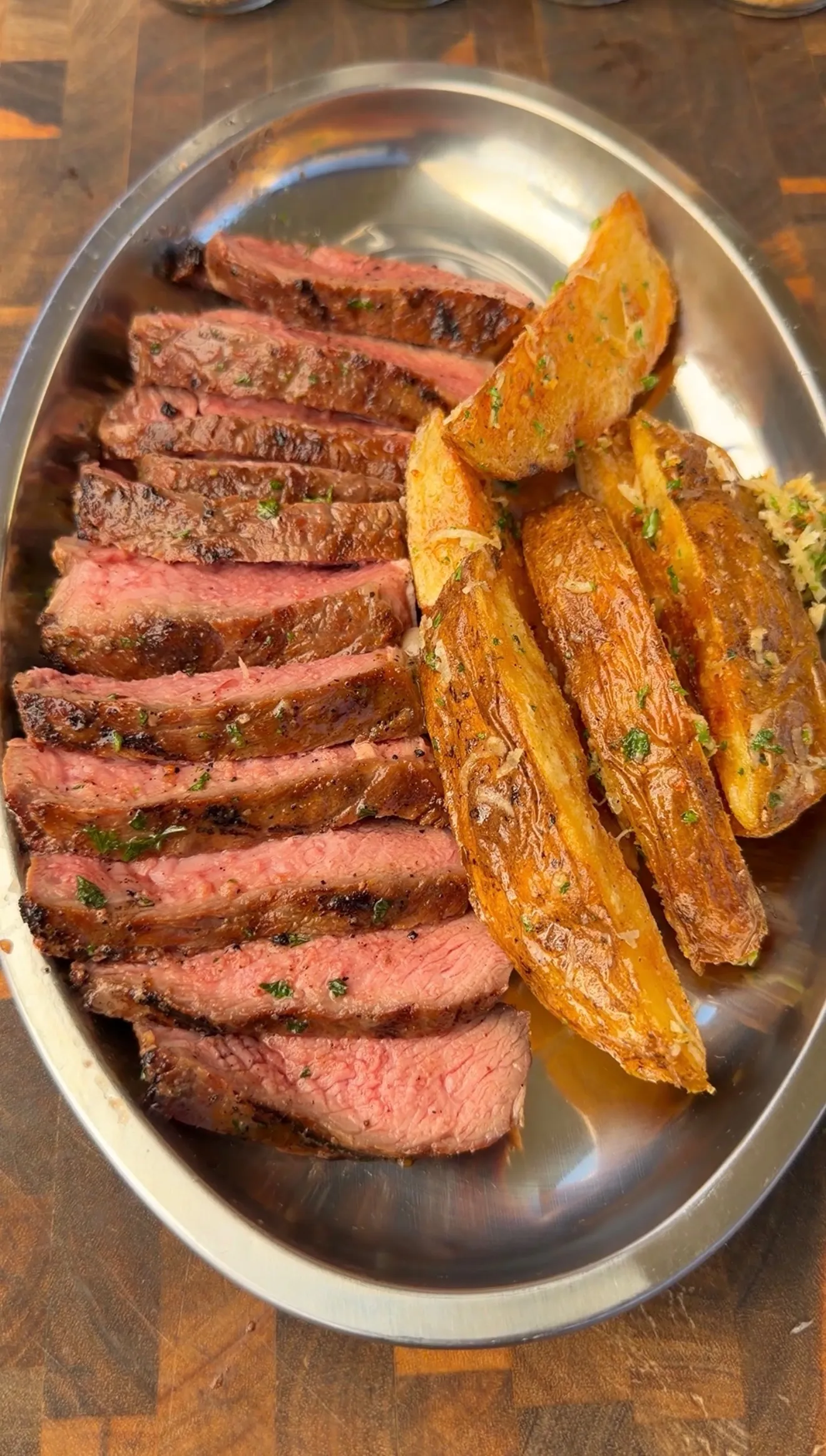 Sliced umami butter grilled ribeye steak cooked medium-rare served with crispy parmesan potato wedges on a silver platter