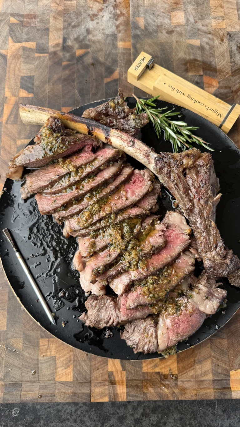 Sliced tomahawk ribeye steak topped with chimichurri sauce on a black cast iron plate with fresh rosemary