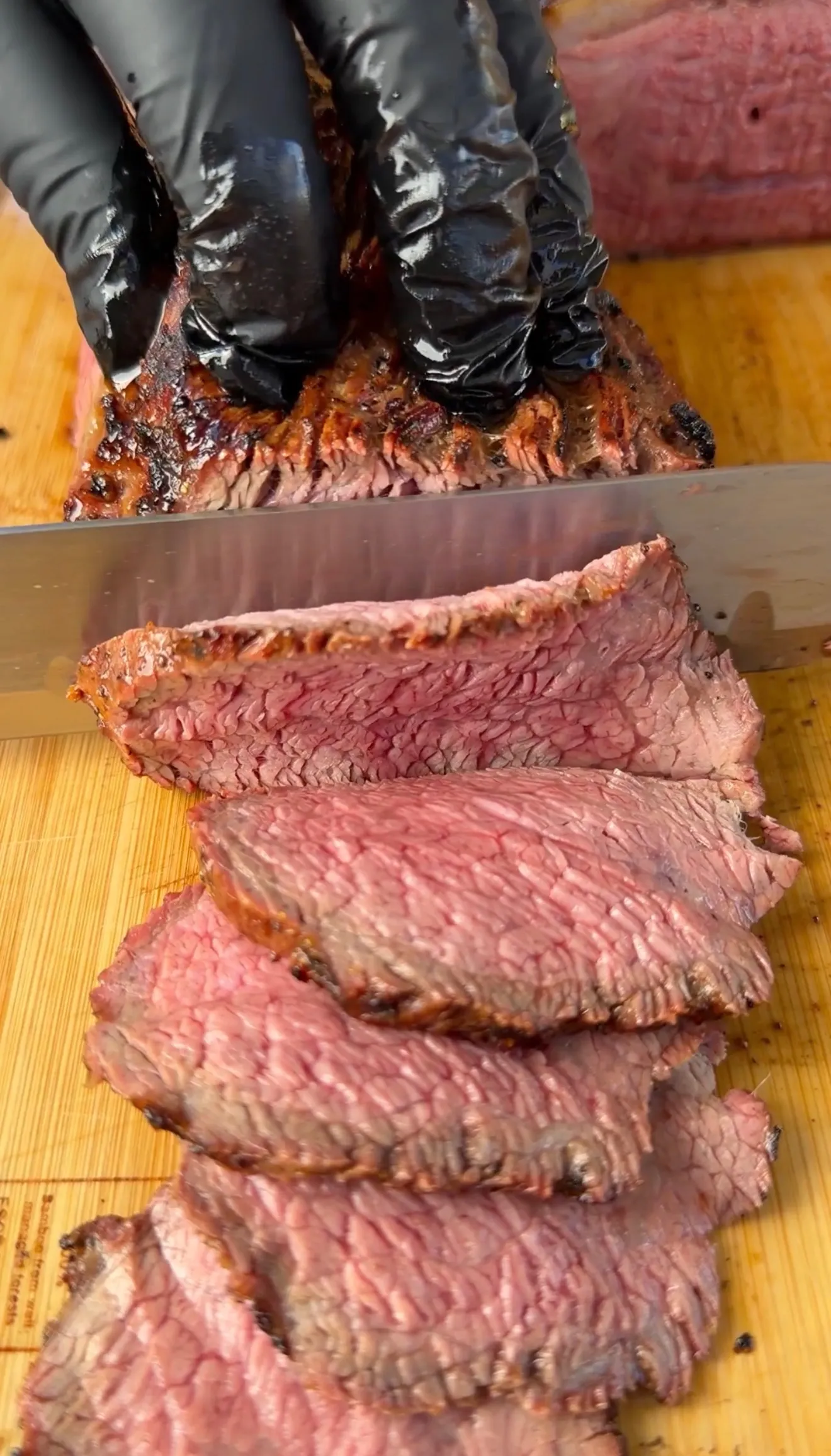 Hands in black gloves slicing smoked tri-tip into tender pink cuts on a wooden cutting board