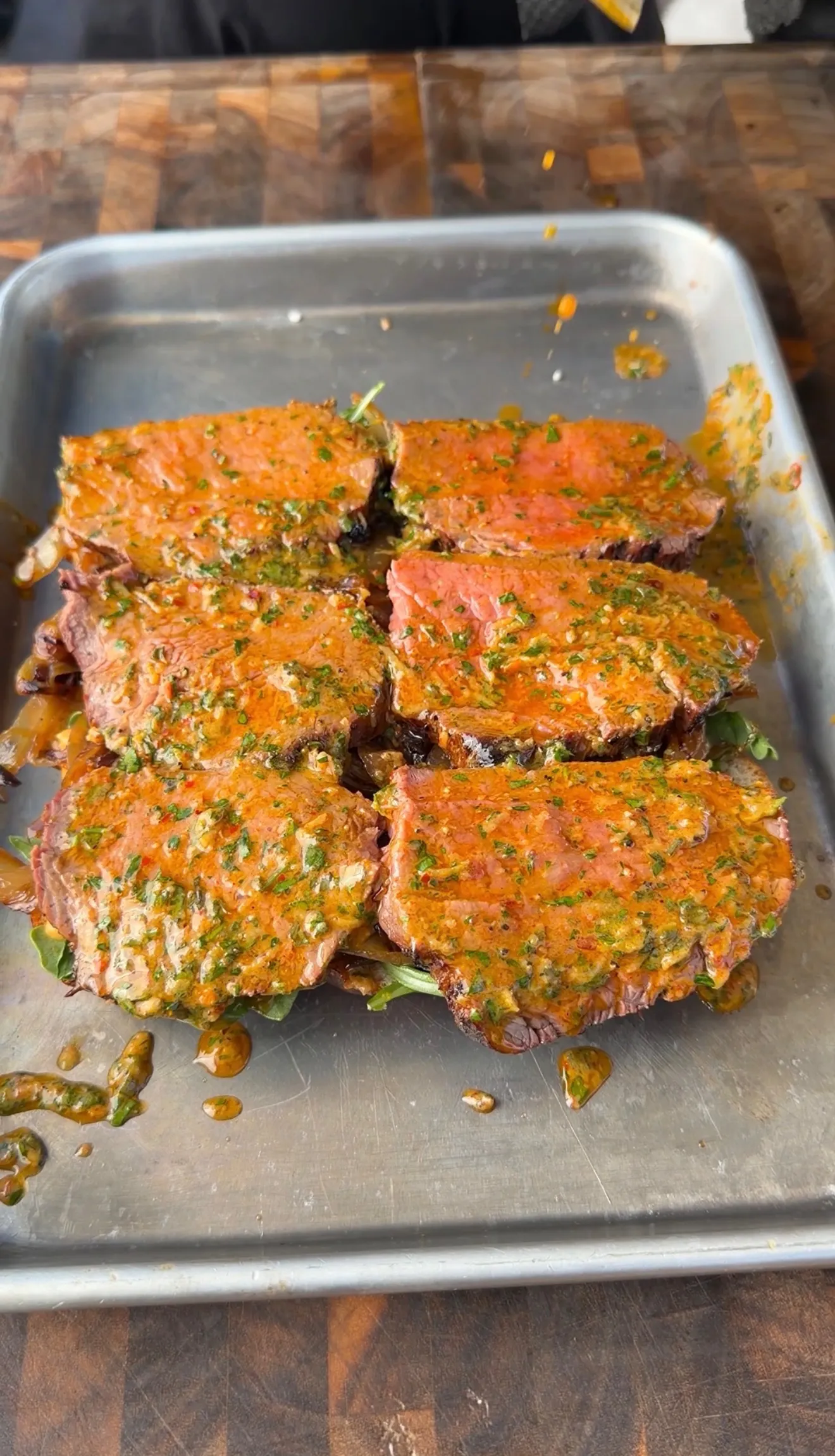 Sliced tri-tip steaks coated in herbed cowboy butter sauce arranged in a stainless steel pan