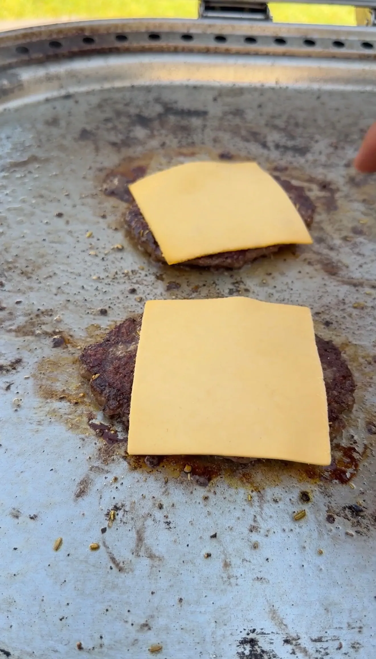 Two smashed burger patties topped with melting American cheese slices cooking on a flat top griddle