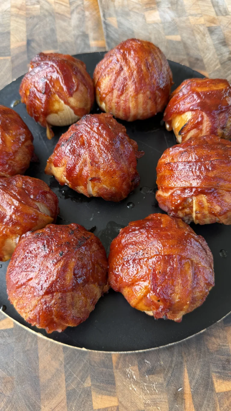 Nine BBQ-glazed smoked bacon-wrapped onion bombs arranged on a dark round plate on a wooden cutting board