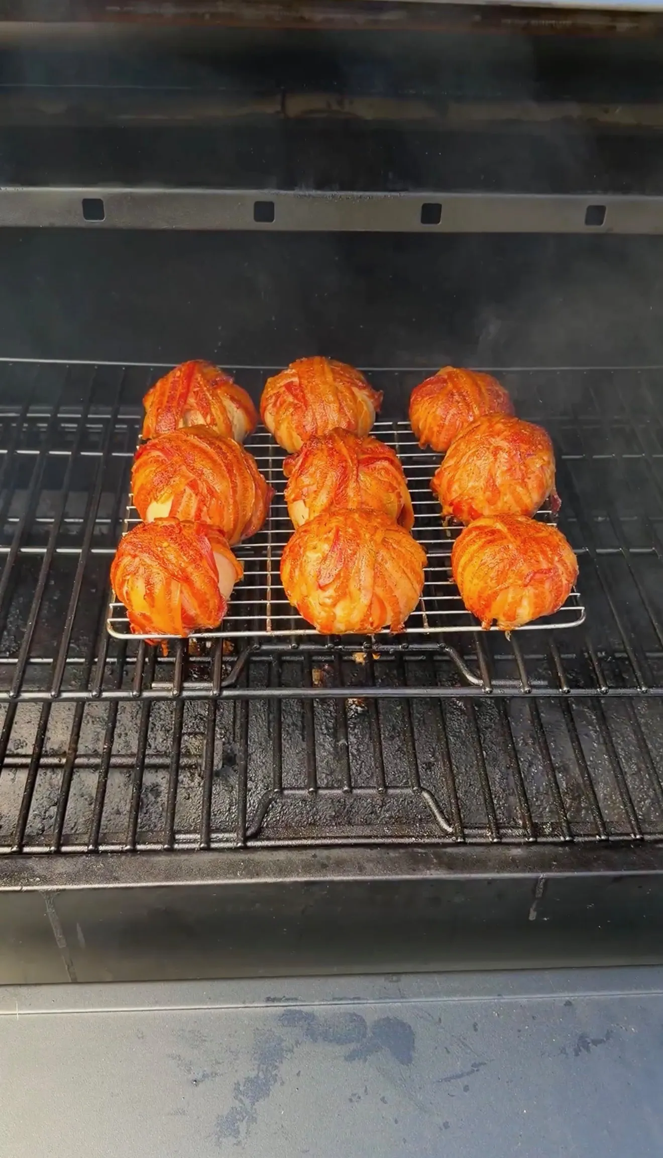 Nine bacon-wrapped onion bombs coated in BBQ sauce smoking on a wire rack inside a pellet smoker