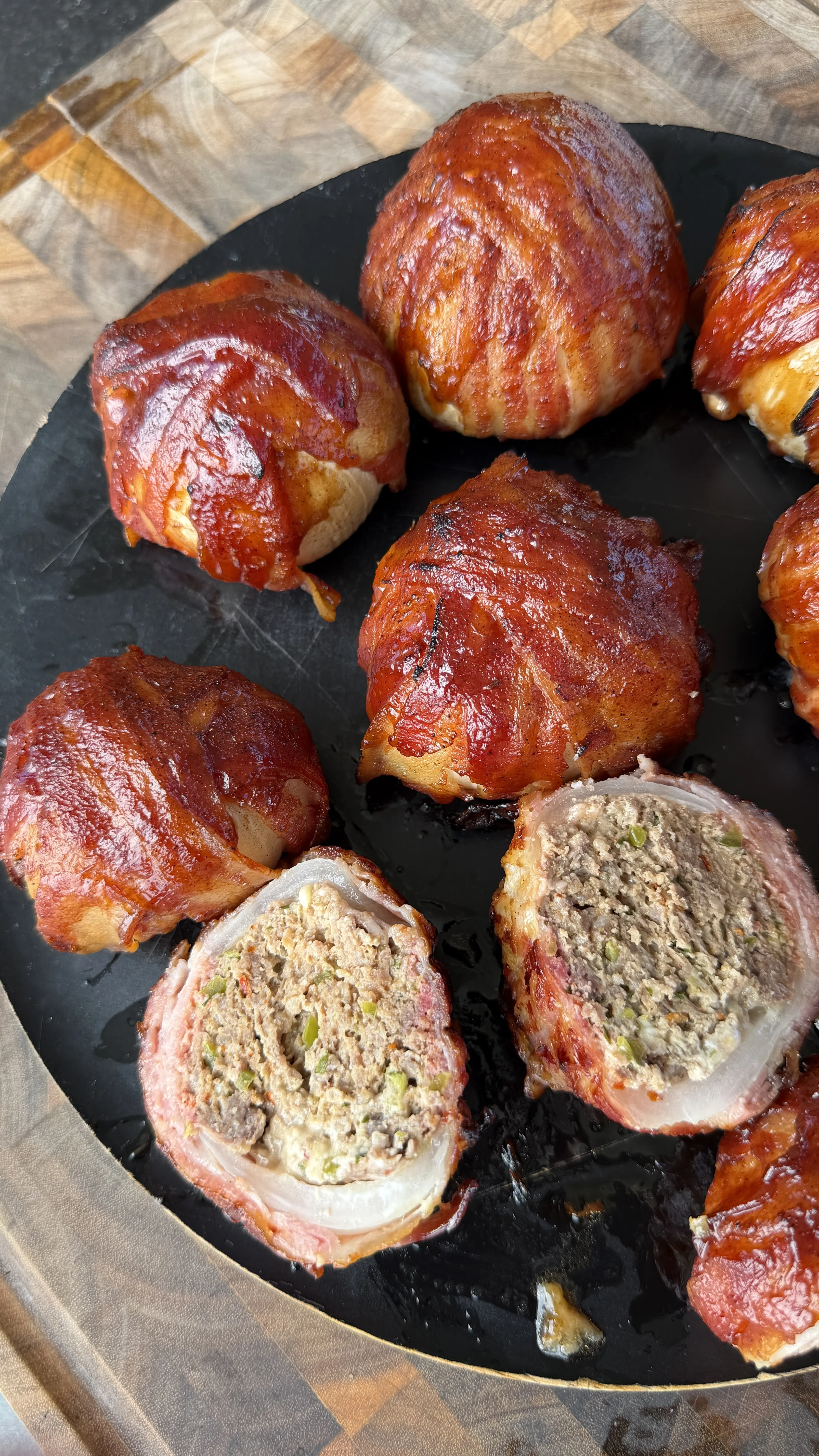 Smoked bacon-wrapped onion bombs on a black plate, one cut open revealing the seasoned meat filling