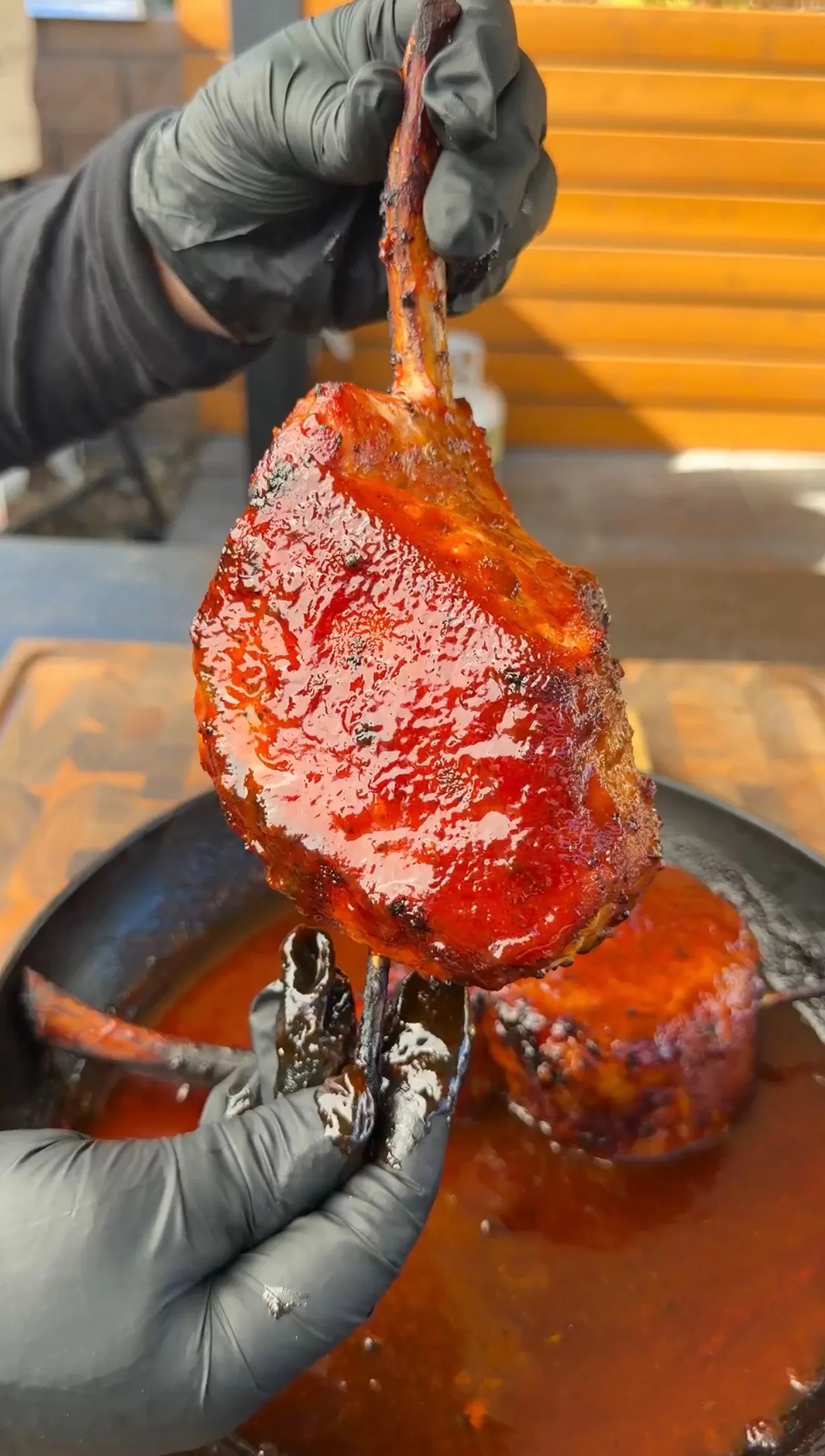 Glazed smoked tomahawk pork chop dripping with black raspberry BBQ sauce held over cast iron pan