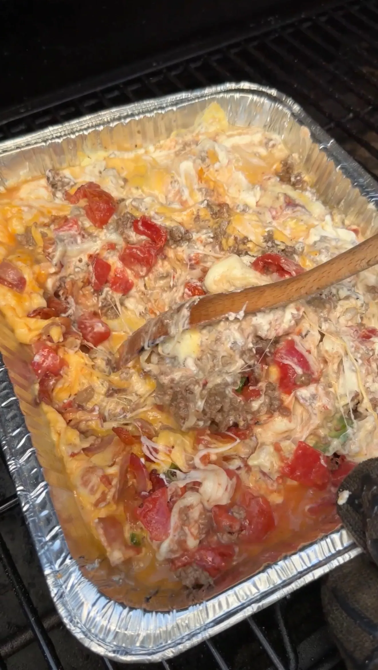 Smoked cheeseburger queso dip with melted cheese, ground beef, and tomatoes in a foil pan on a grill