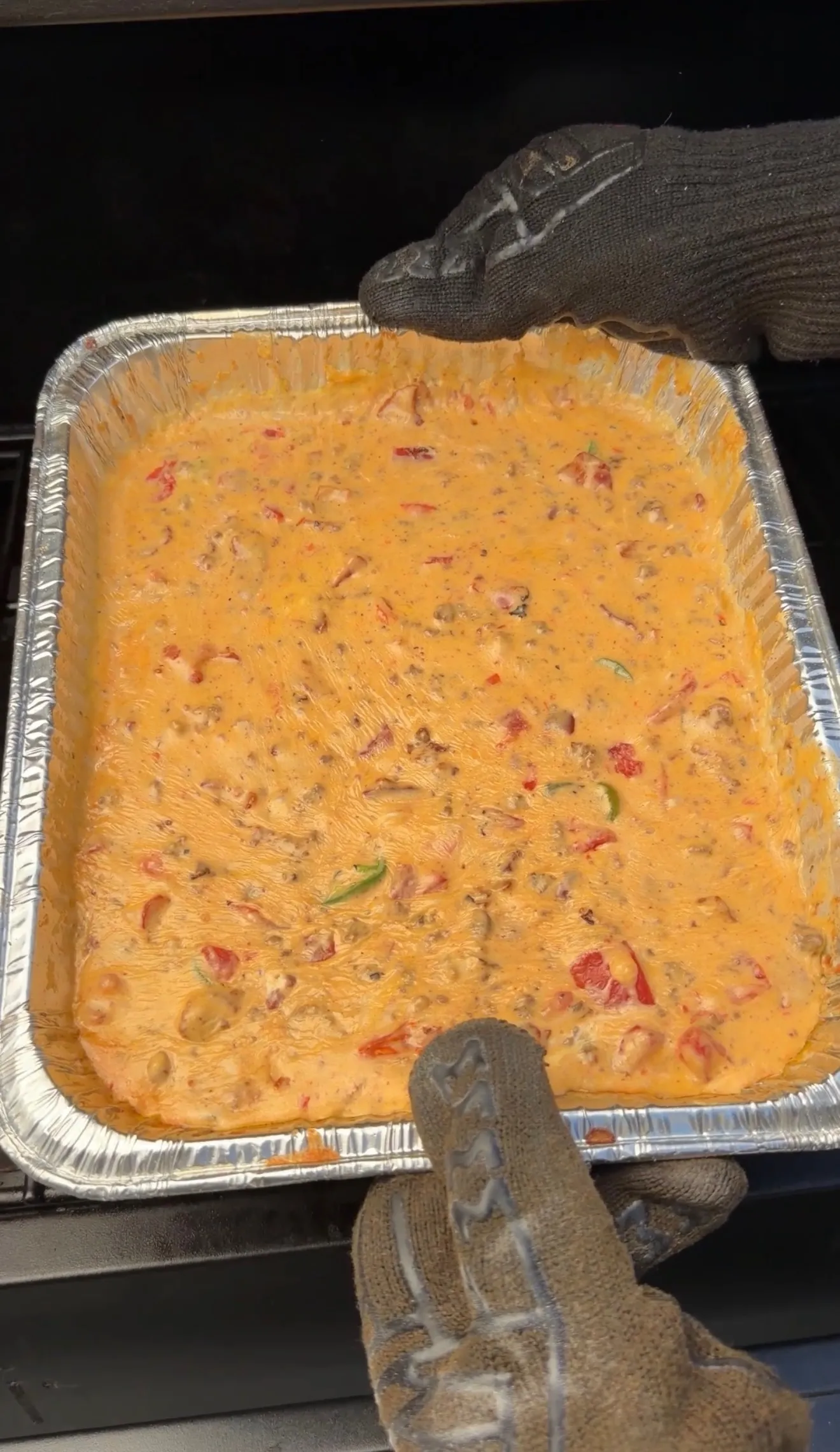 Creamy smoked cheeseburger queso dip with peppers and ground beef in a foil pan on a smoker